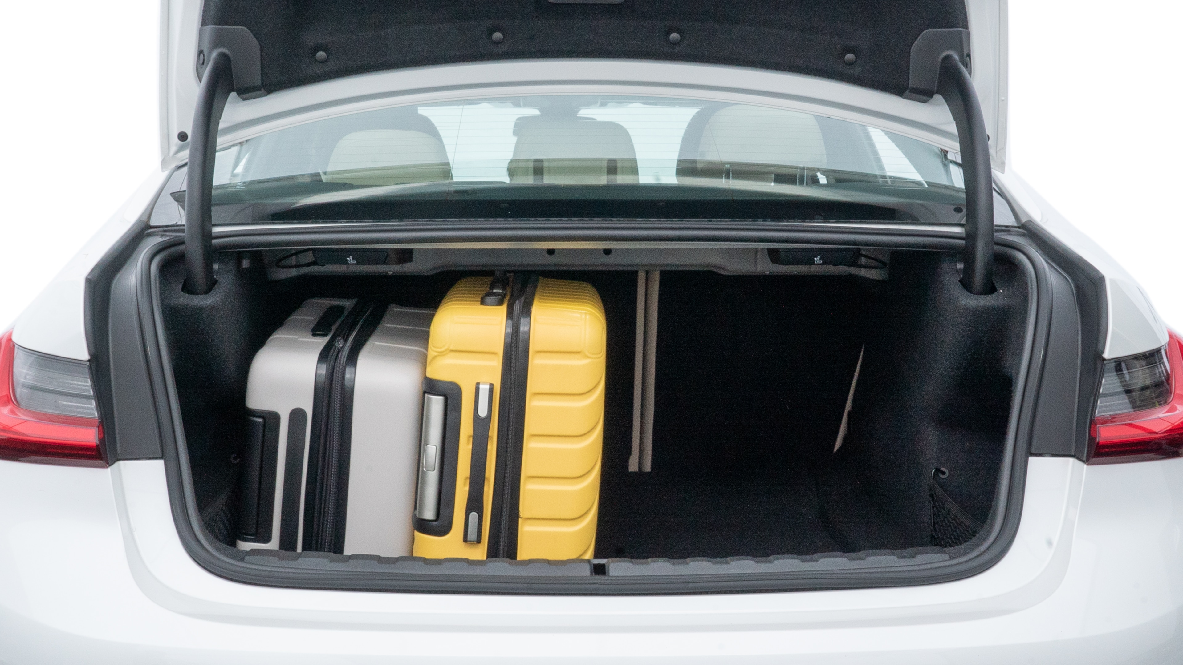 The trunk lid is open, showing full view of the trunk space. One large, two medium, and two small suitcases are placed inside.