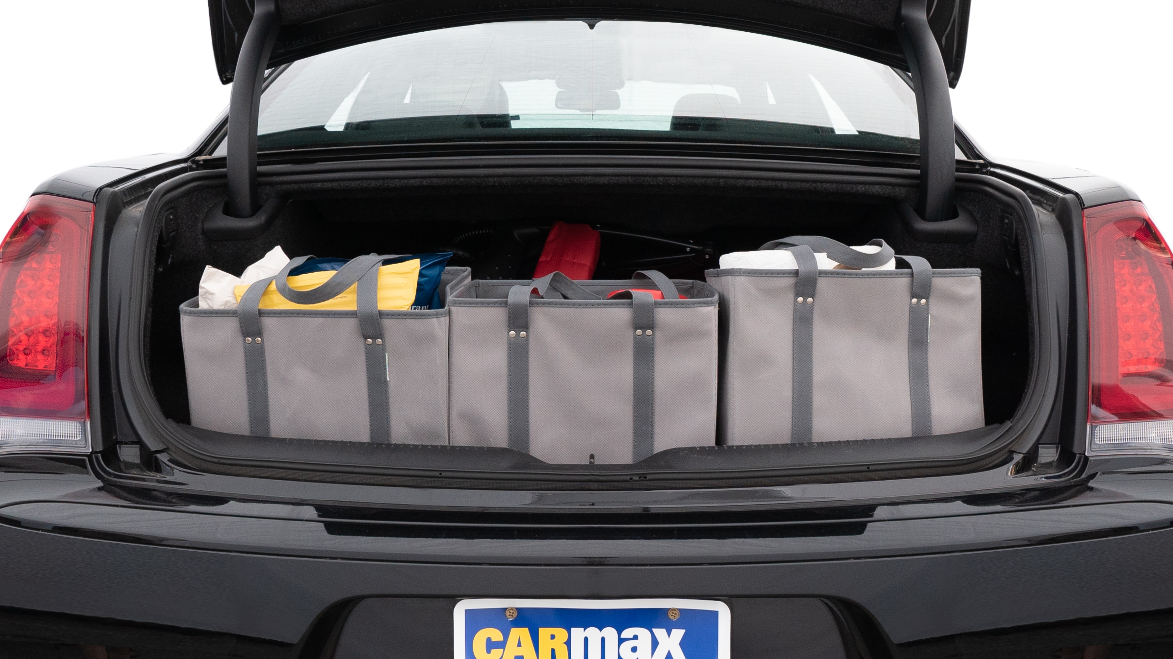 The trunk lid is open showing full view of the trunk. A baby stroller, three grocery carriers, two camping chairs in the carrying bag, and a set of golf clubs are placed inside.