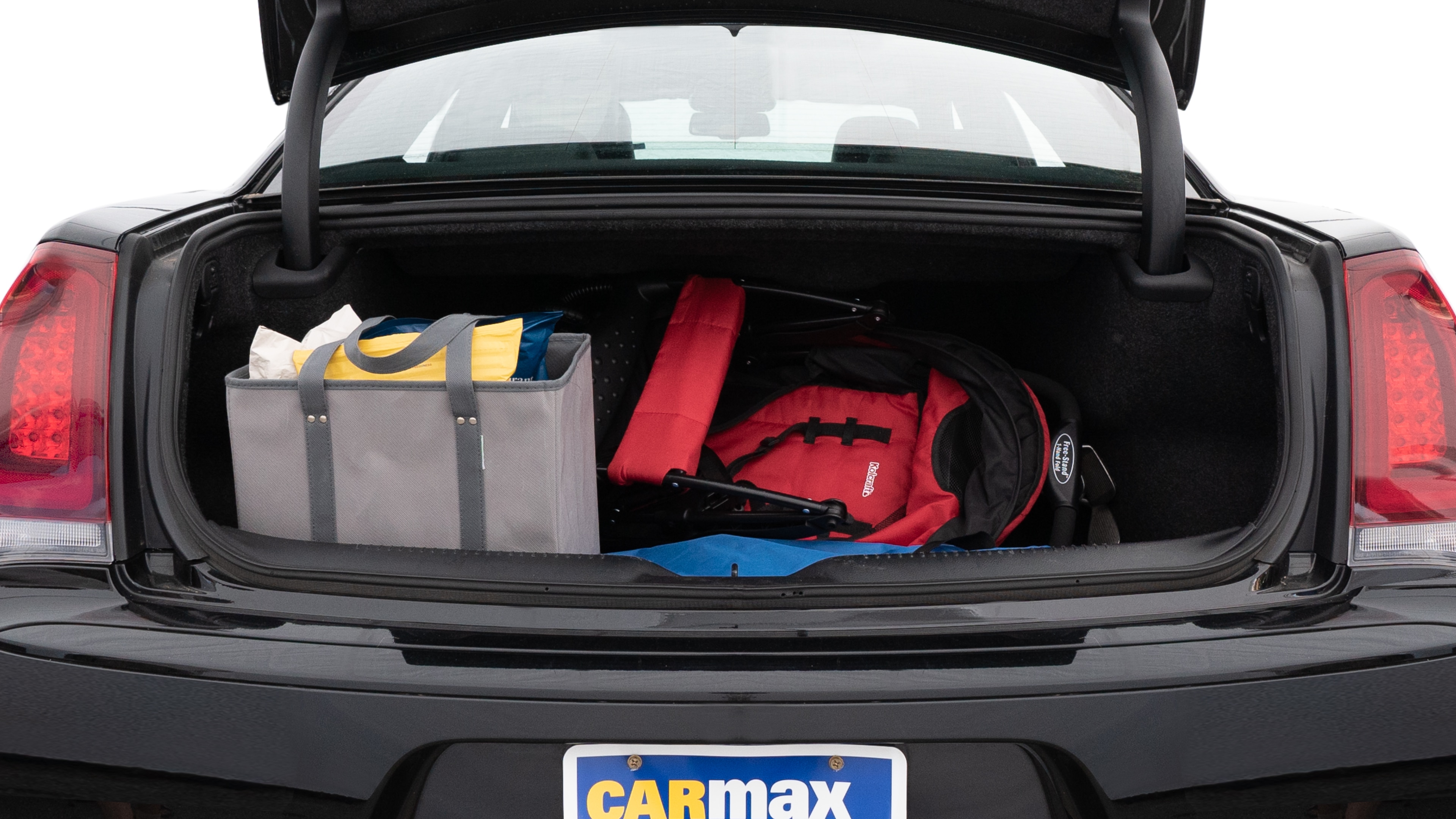 The trunk lid is open showing full view of the trunk. A baby stroller, three grocery carriers, two camping chairs in the carrying bag, and a set of golf clubs are placed inside.
