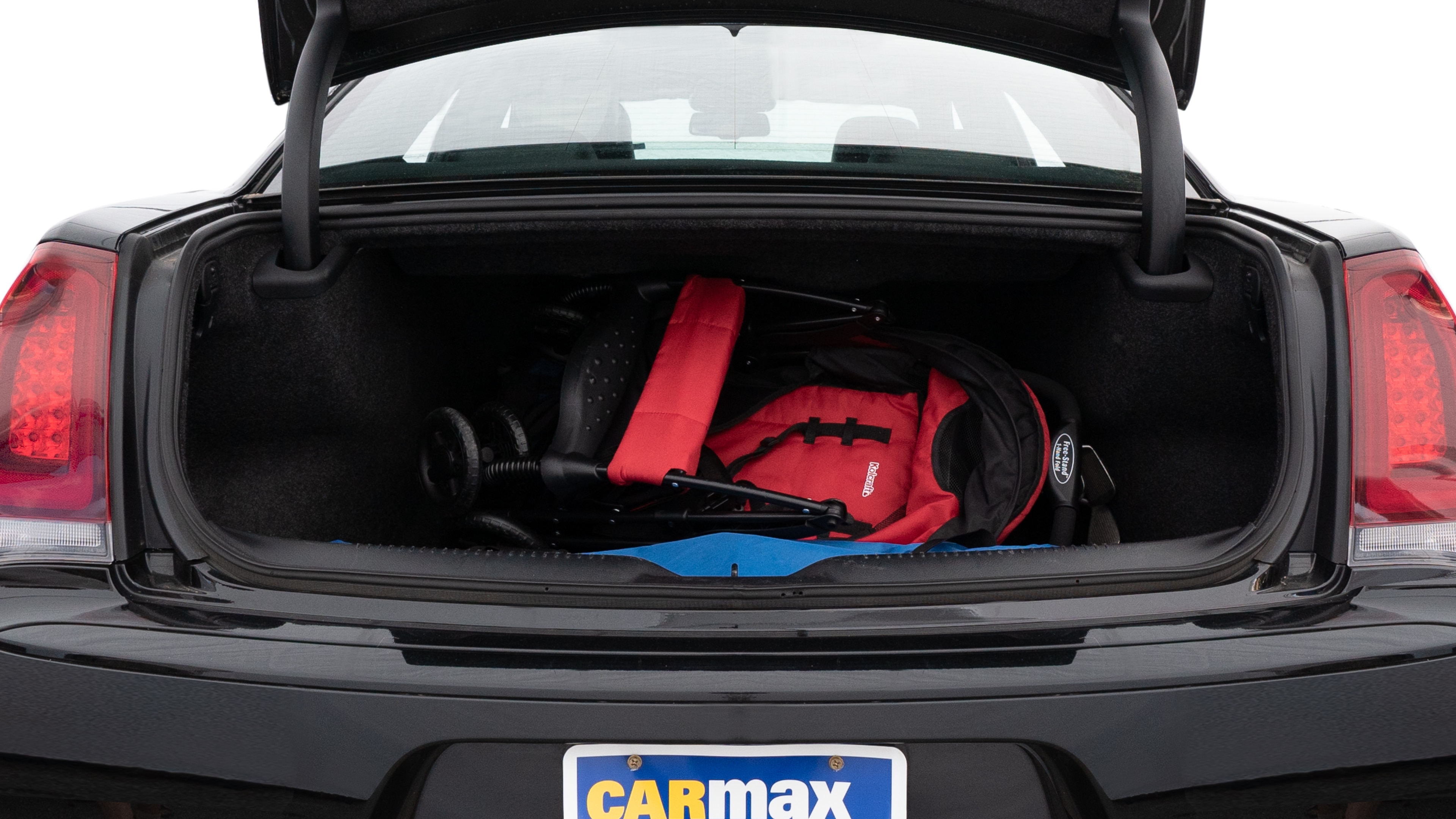 The trunk lid is open showing full view of the trunk. A baby stroller, three grocery carriers, two camping chairs in the carrying bag, and a set of golf clubs are placed inside.