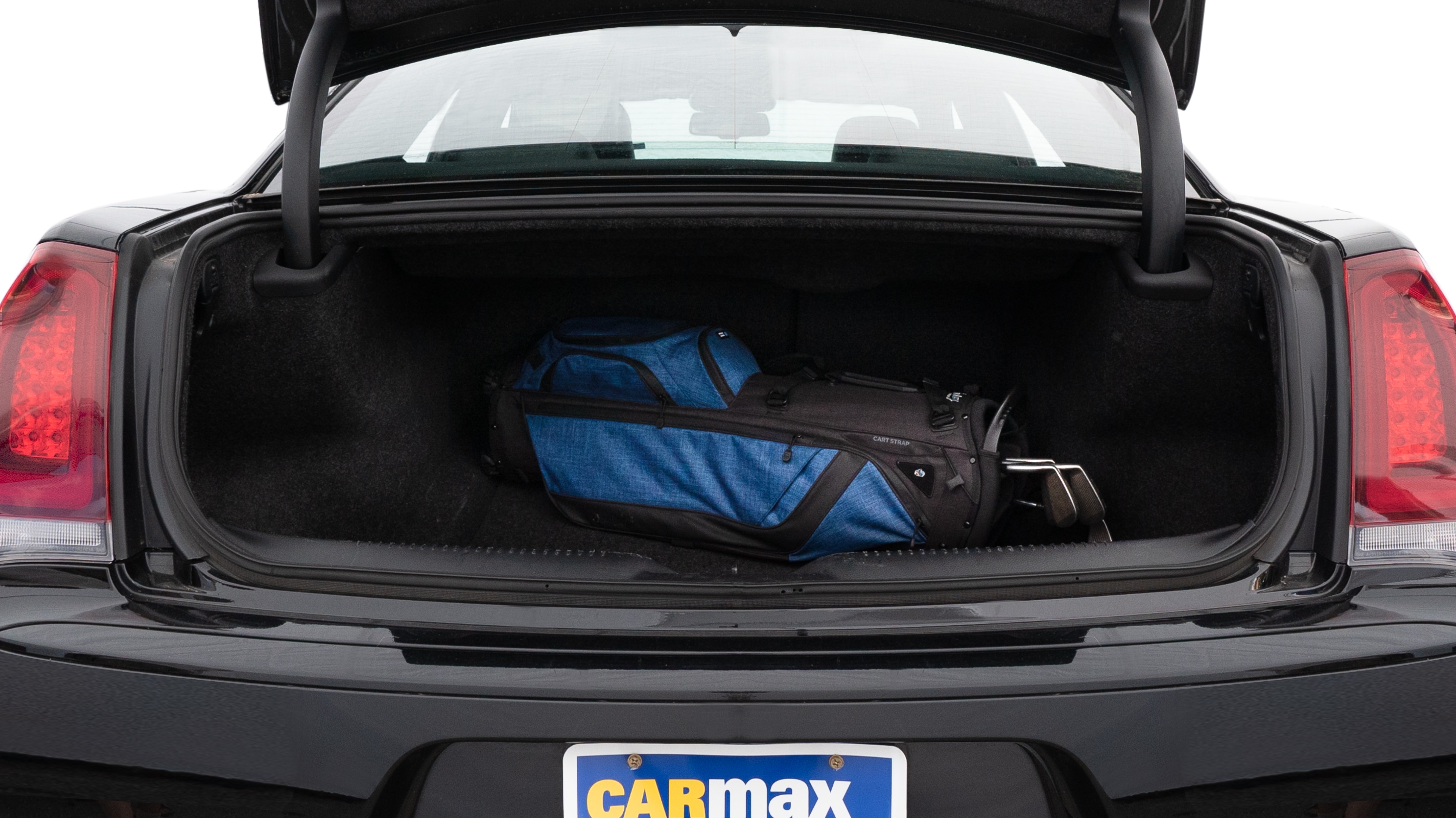 The trunk lid is open showing full view of the trunk. A baby stroller, three grocery carriers, two camping chairs in the carrying bag, and a set of golf clubs are placed inside.