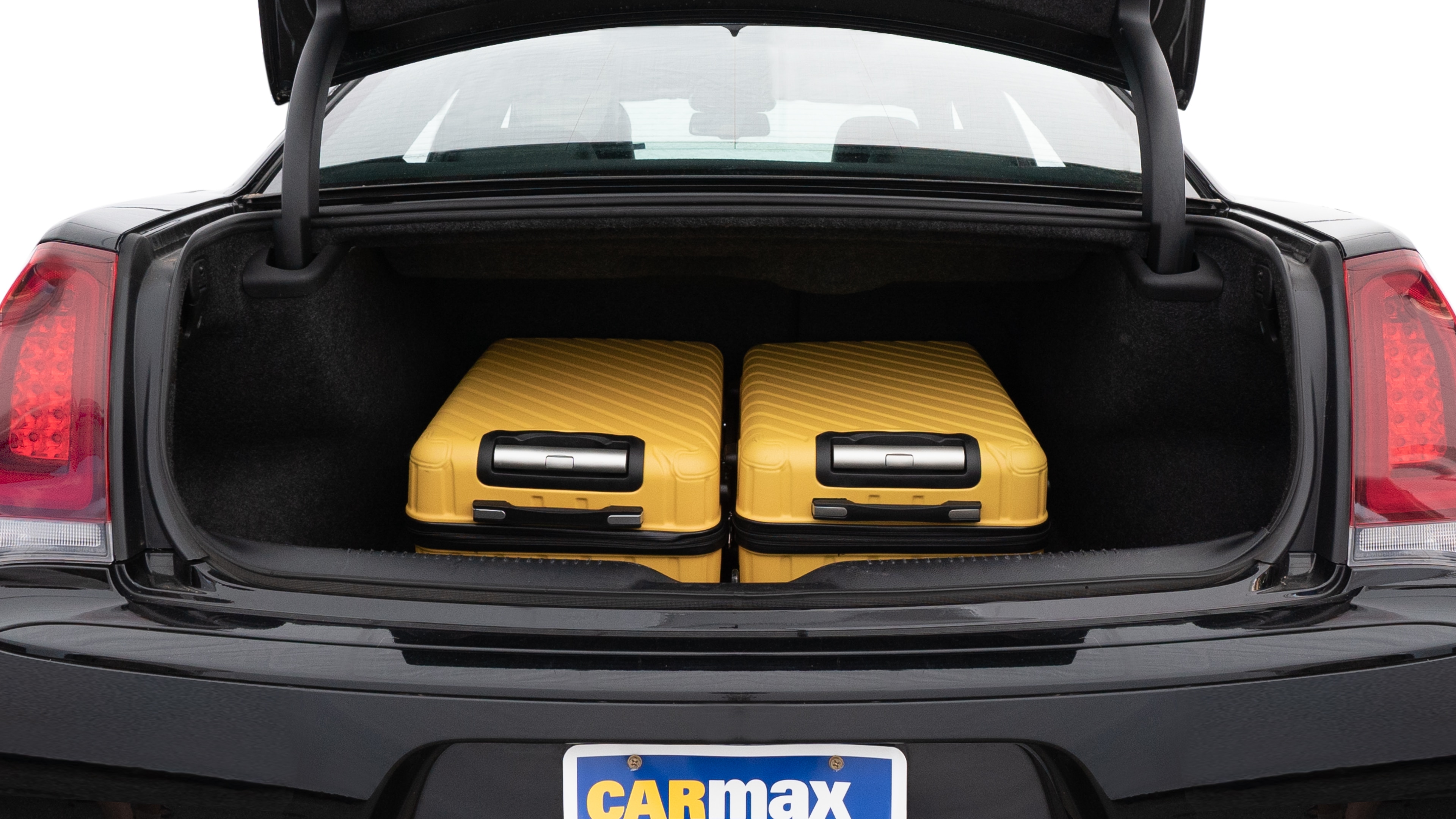 The trunk lid is open, showing full view of the trunk space. One large and two medium suitcases are placed inside.