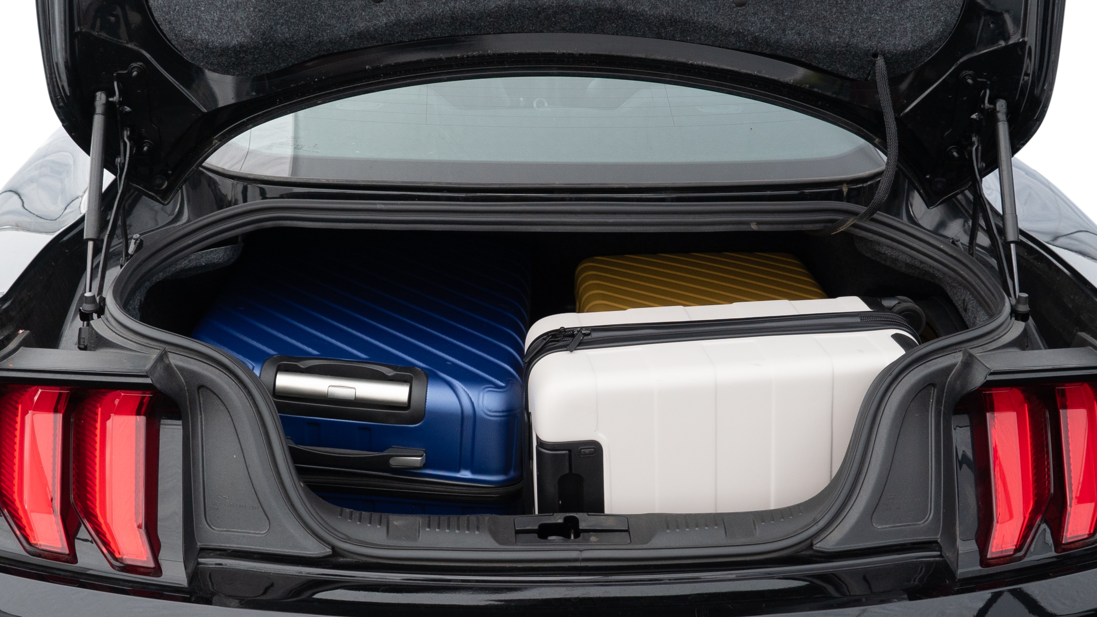 The trunk lid is open, showing full view of the trunk space. One large, one medium, and one small suitcase are placed inside.