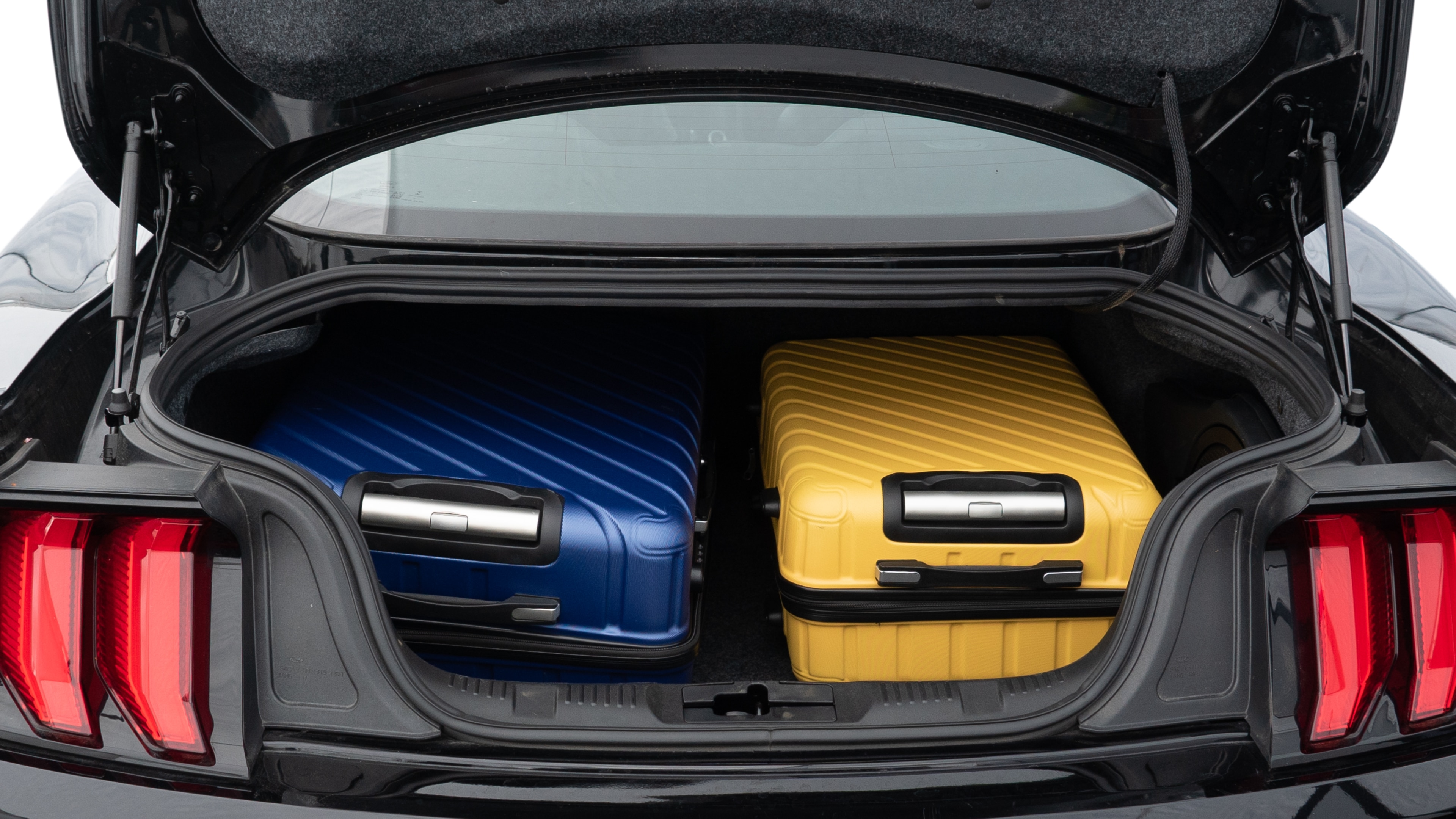 The trunk lid is open, showing full view of the trunk space. One large, one medium, and one small suitcase are placed inside.