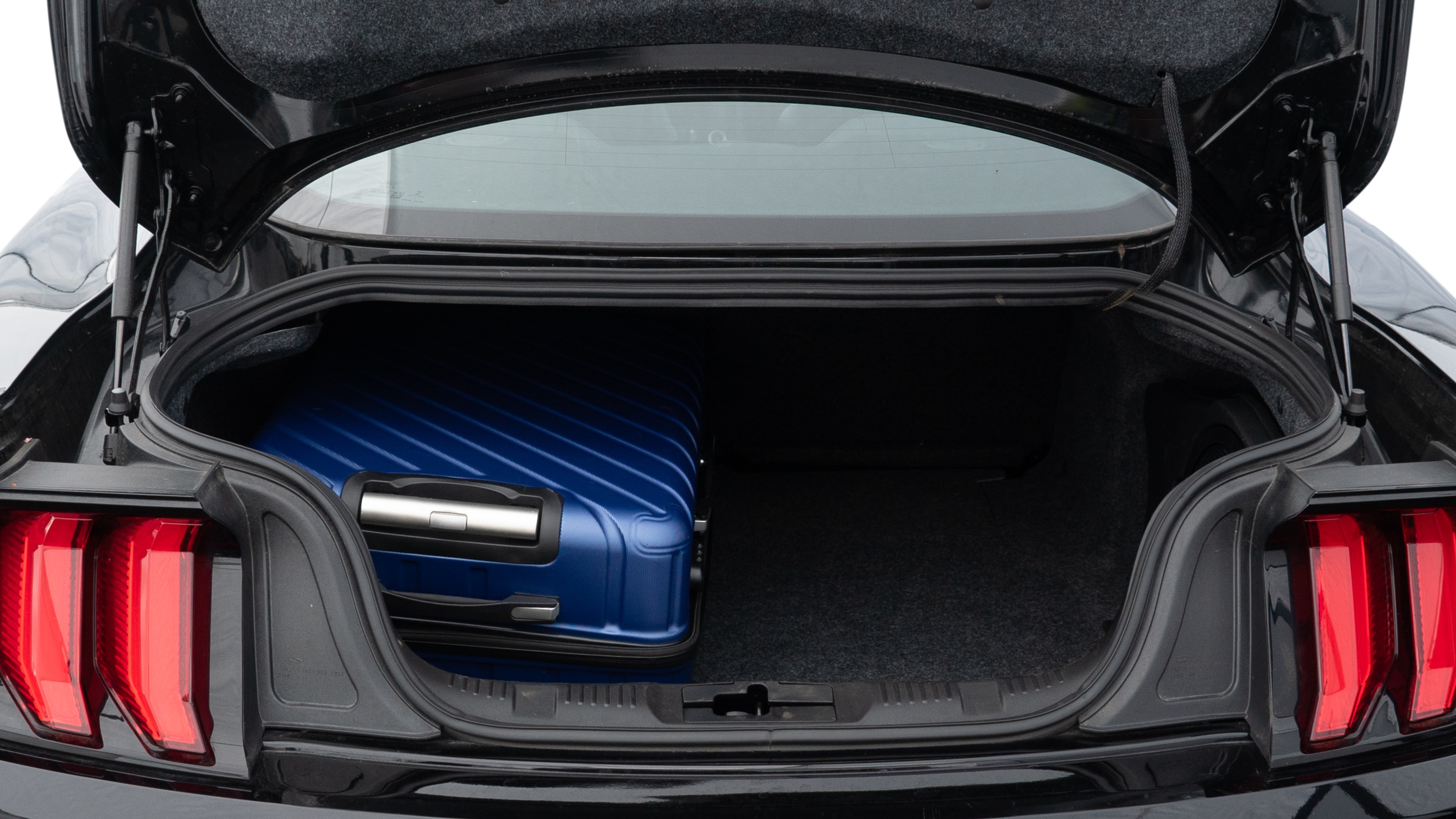 The trunk lid is open, showing full view of the trunk space. One large, one medium, and one small suitcase are placed inside.