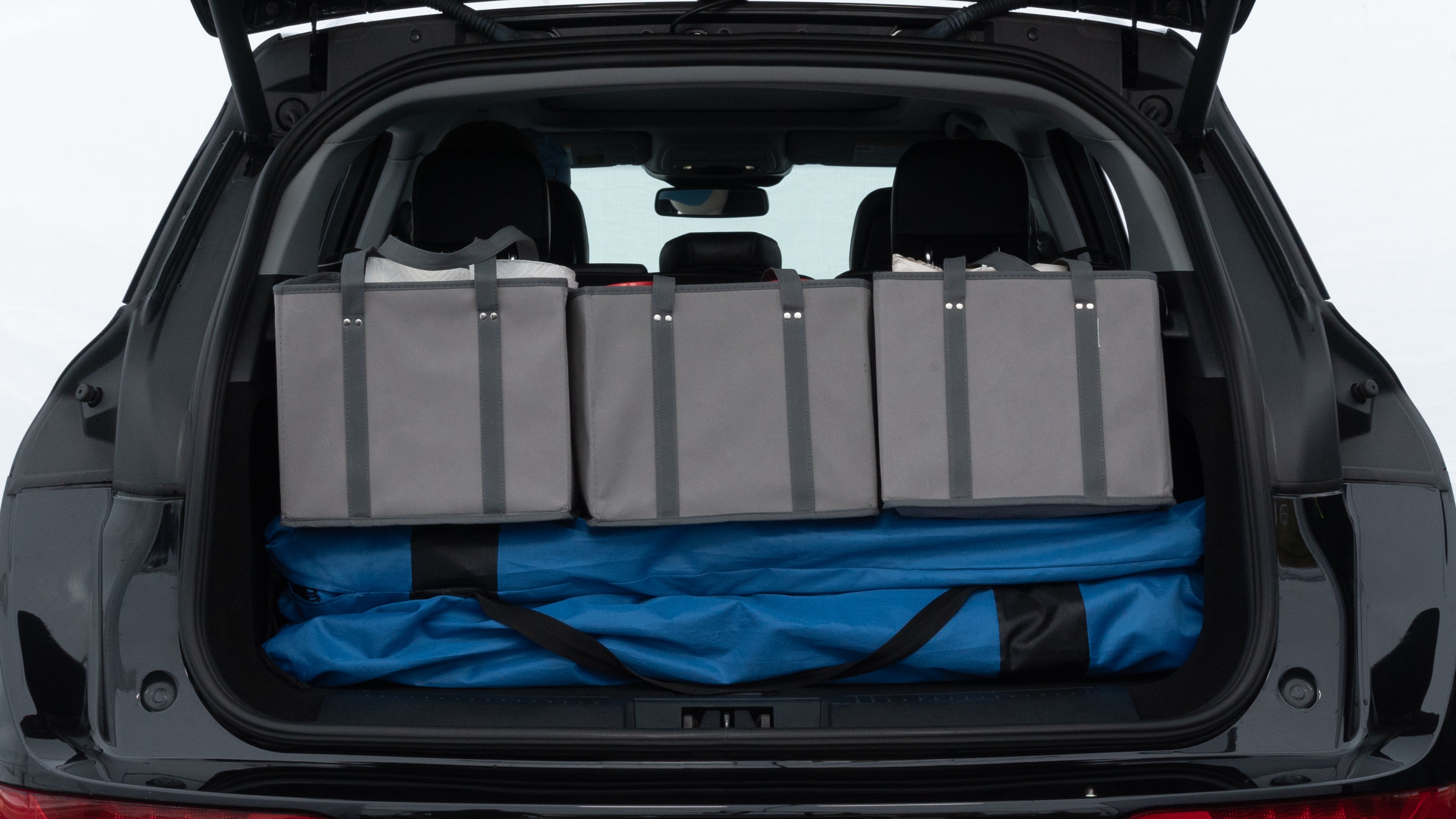 The trunk lid is open showing full view of the trunk. A baby stroller, three grocery carriers, two camping chairs in the carrying bag, and a set of golf clubs are placed inside.