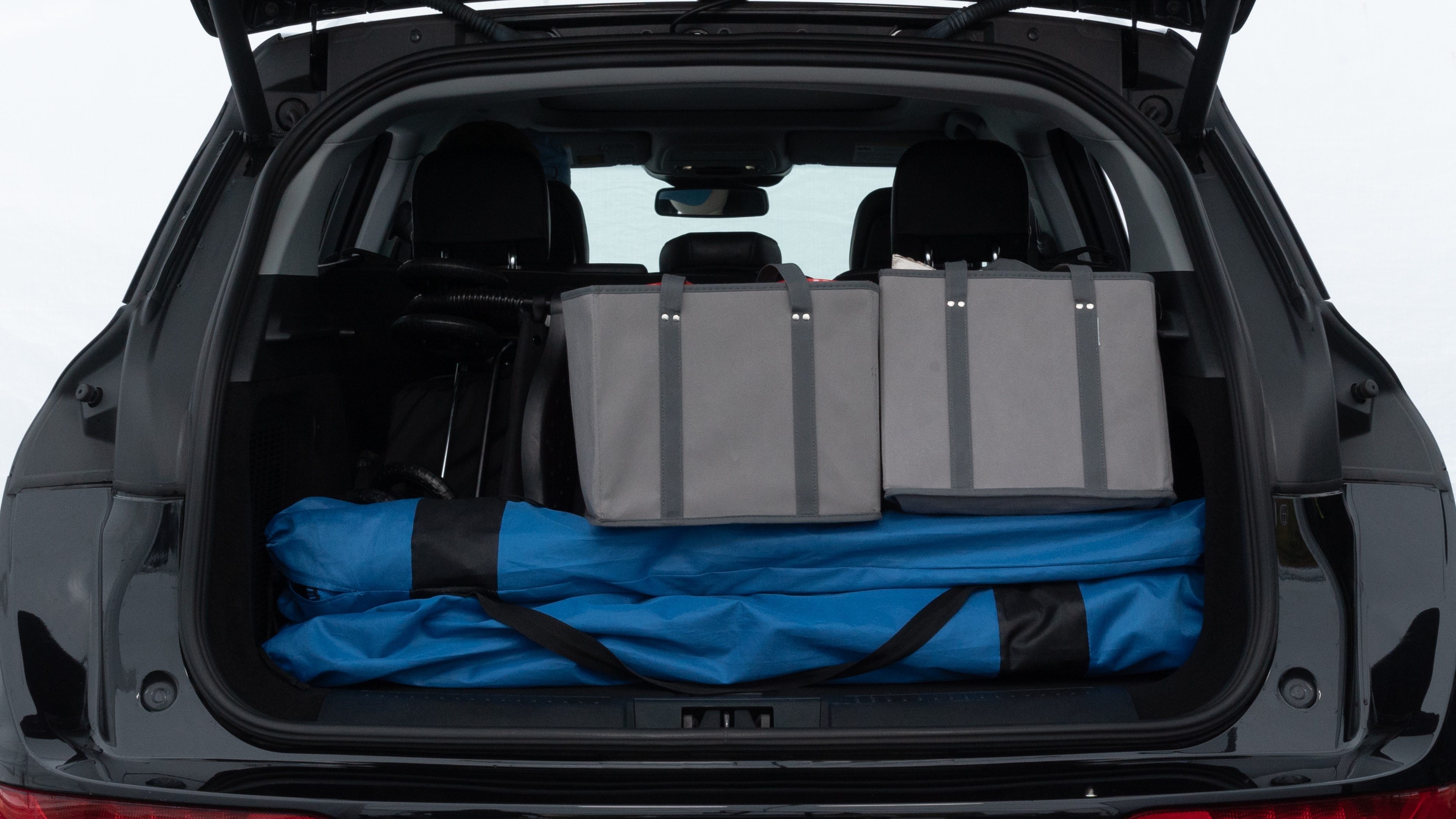 The trunk lid is open showing full view of the trunk. A baby stroller, three grocery carriers, two camping chairs in the carrying bag, and a set of golf clubs are placed inside.