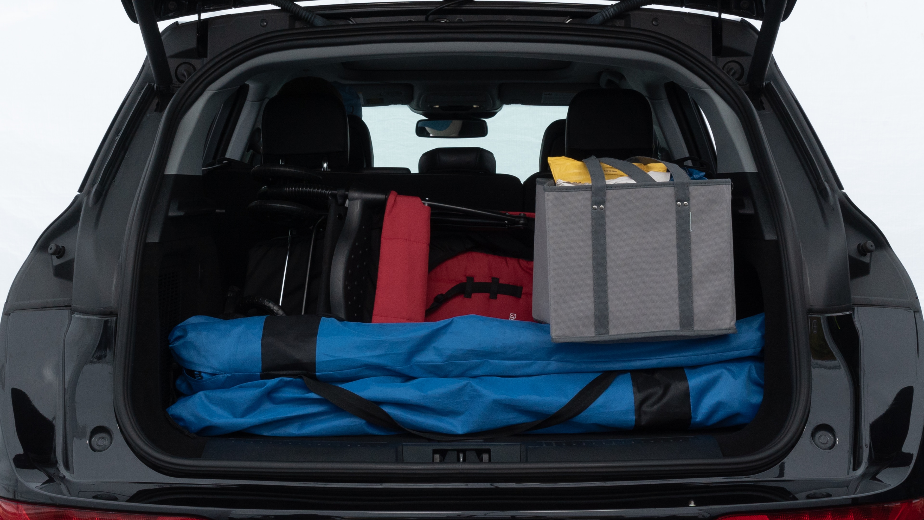 The trunk lid is open showing full view of the trunk. A baby stroller, three grocery carriers, two camping chairs in the carrying bag, and a set of golf clubs are placed inside.