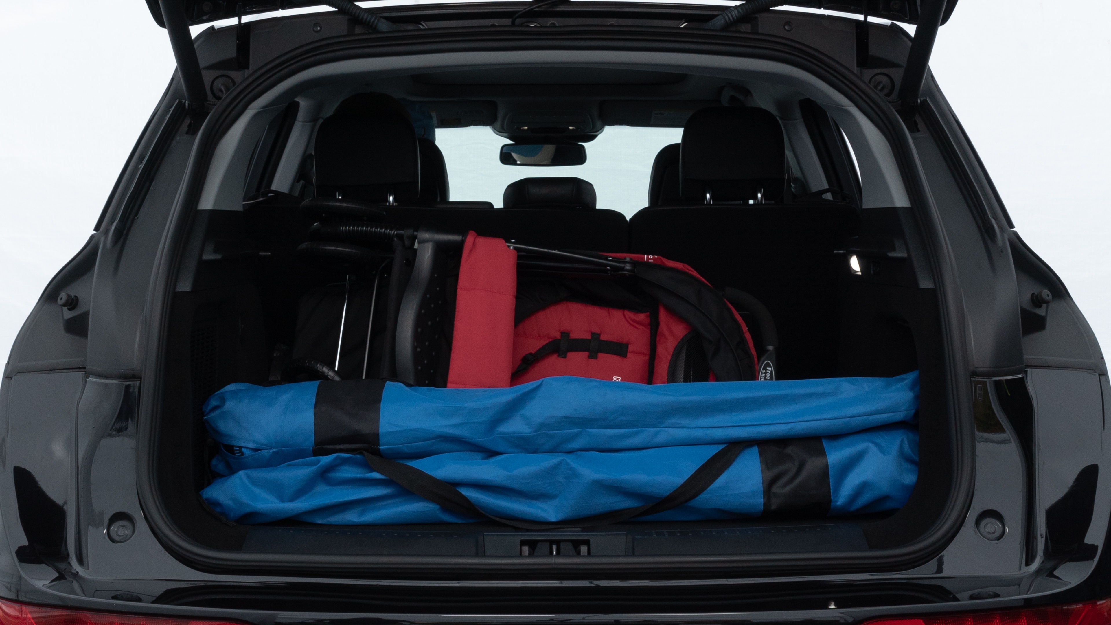 The trunk lid is open showing full view of the trunk. A baby stroller, three grocery carriers, two camping chairs in the carrying bag, and a set of golf clubs are placed inside.