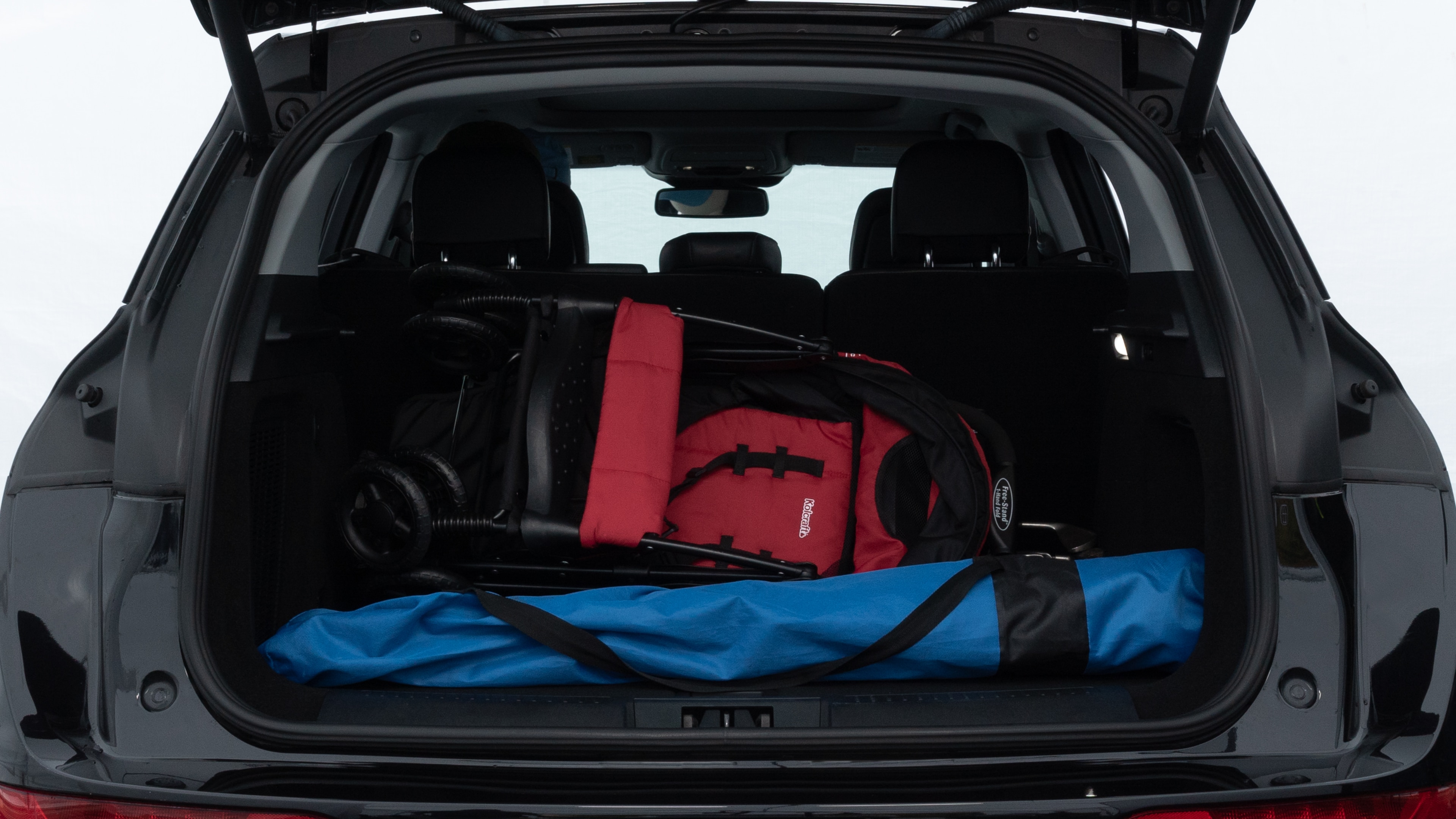 The trunk lid is open showing full view of the trunk. A baby stroller, three grocery carriers, two camping chairs in the carrying bag, and a set of golf clubs are placed inside.