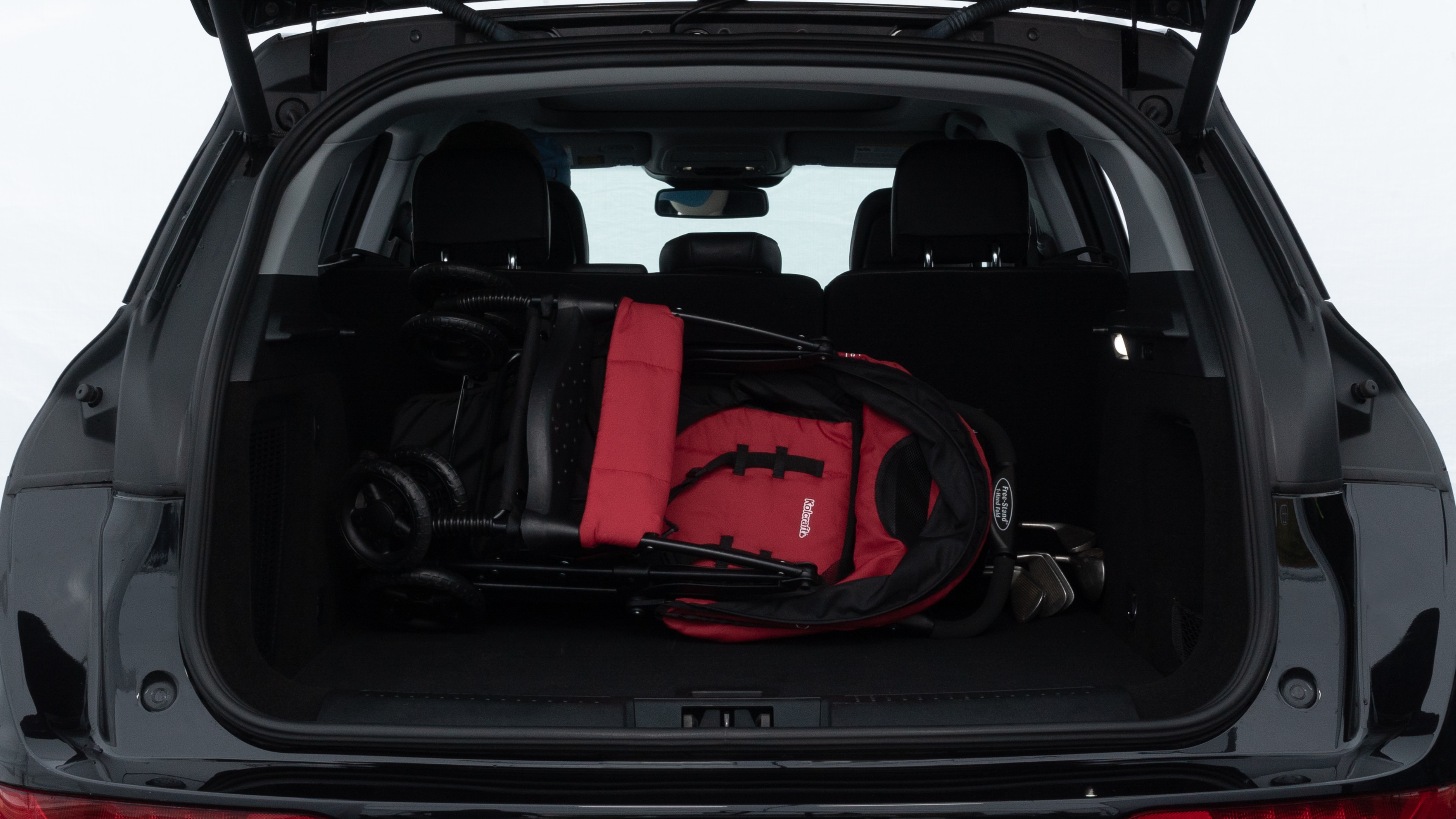 The trunk lid is open showing full view of the trunk. A baby stroller, three grocery carriers, two camping chairs in the carrying bag, and a set of golf clubs are placed inside.