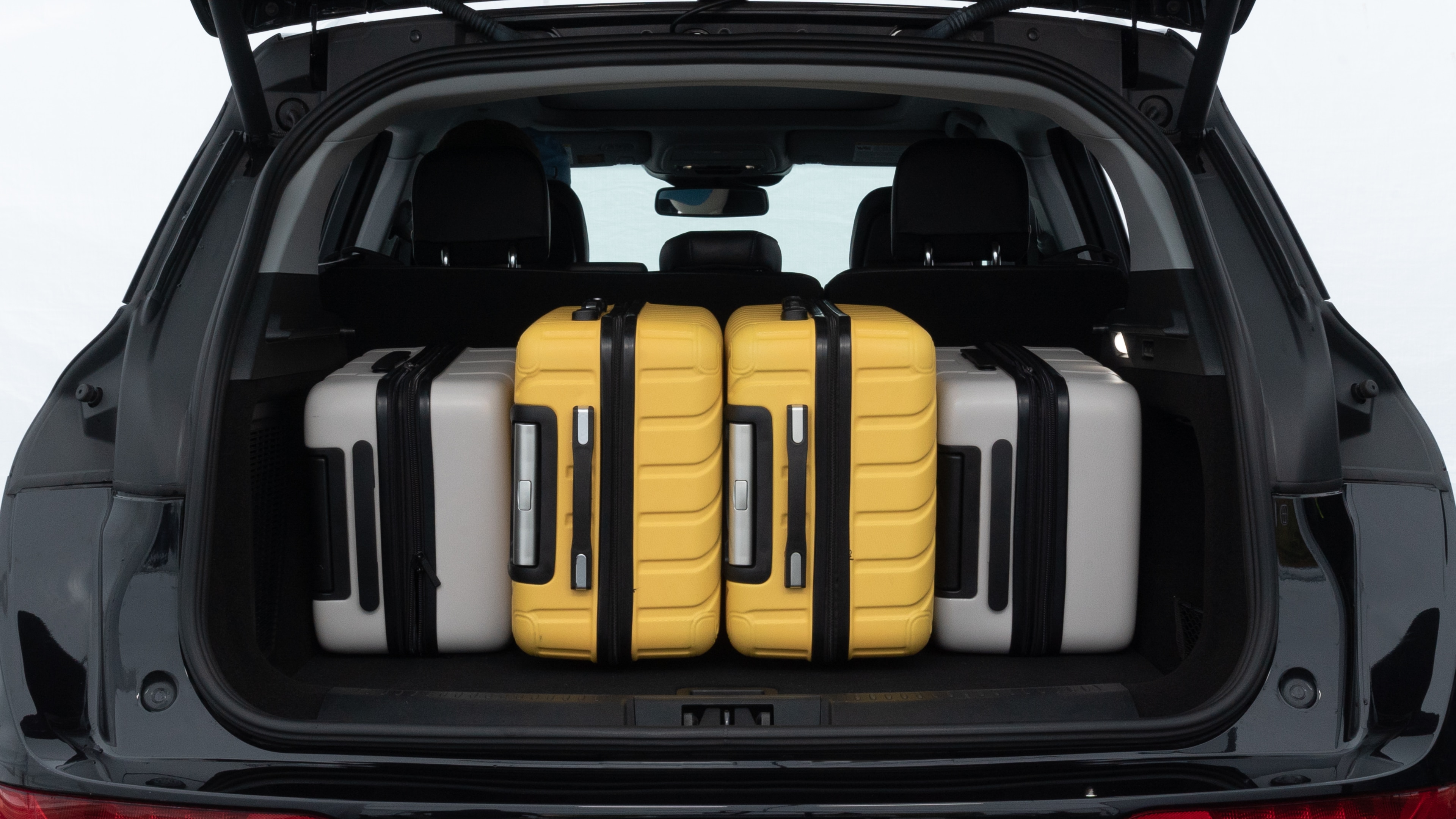 The trunk lid is open, showing full view of the trunk space. Two medium and two small suitcases are placed inside.