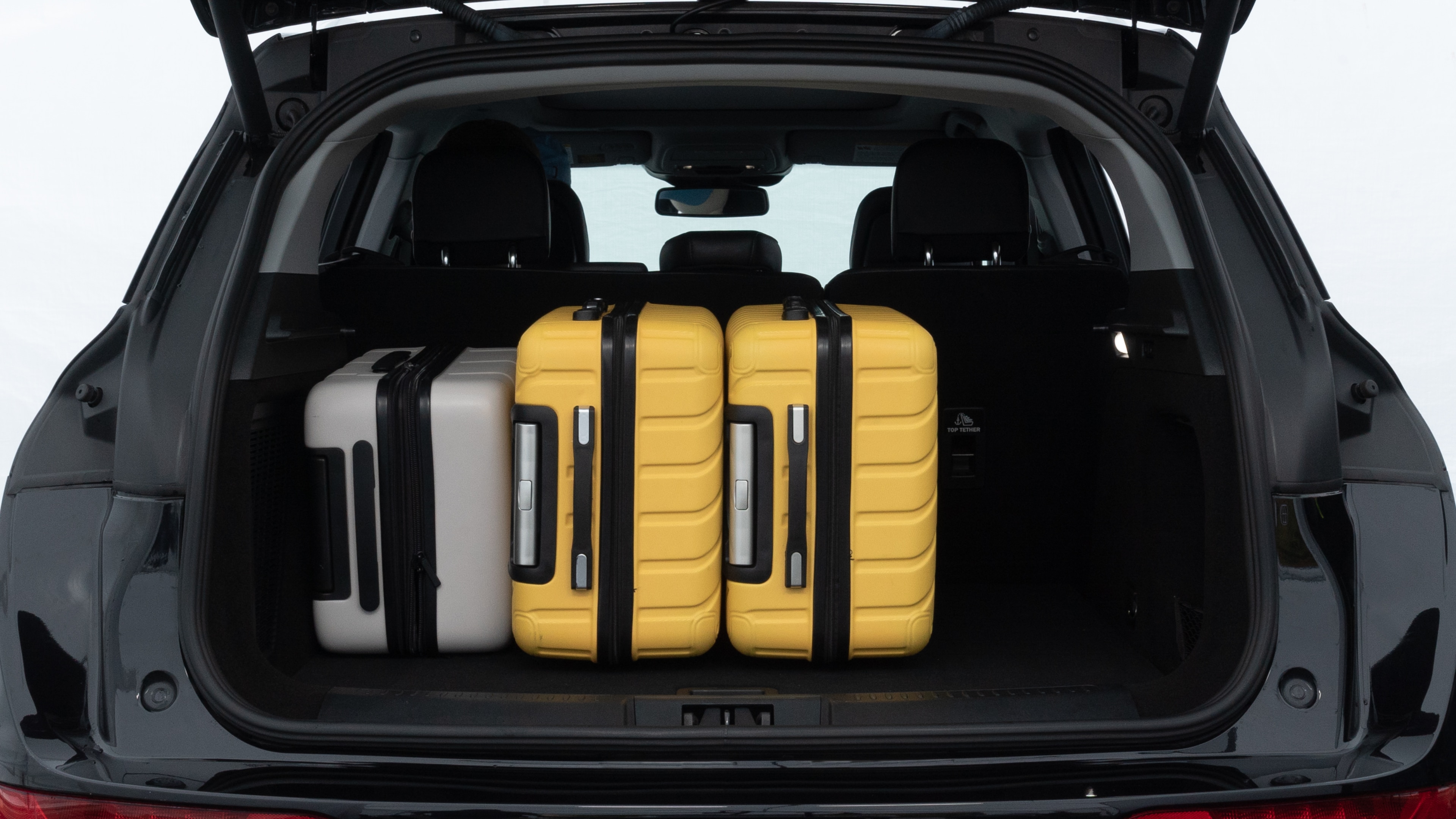 The trunk lid is open, showing full view of the trunk space. Two medium and two small suitcases are placed inside.