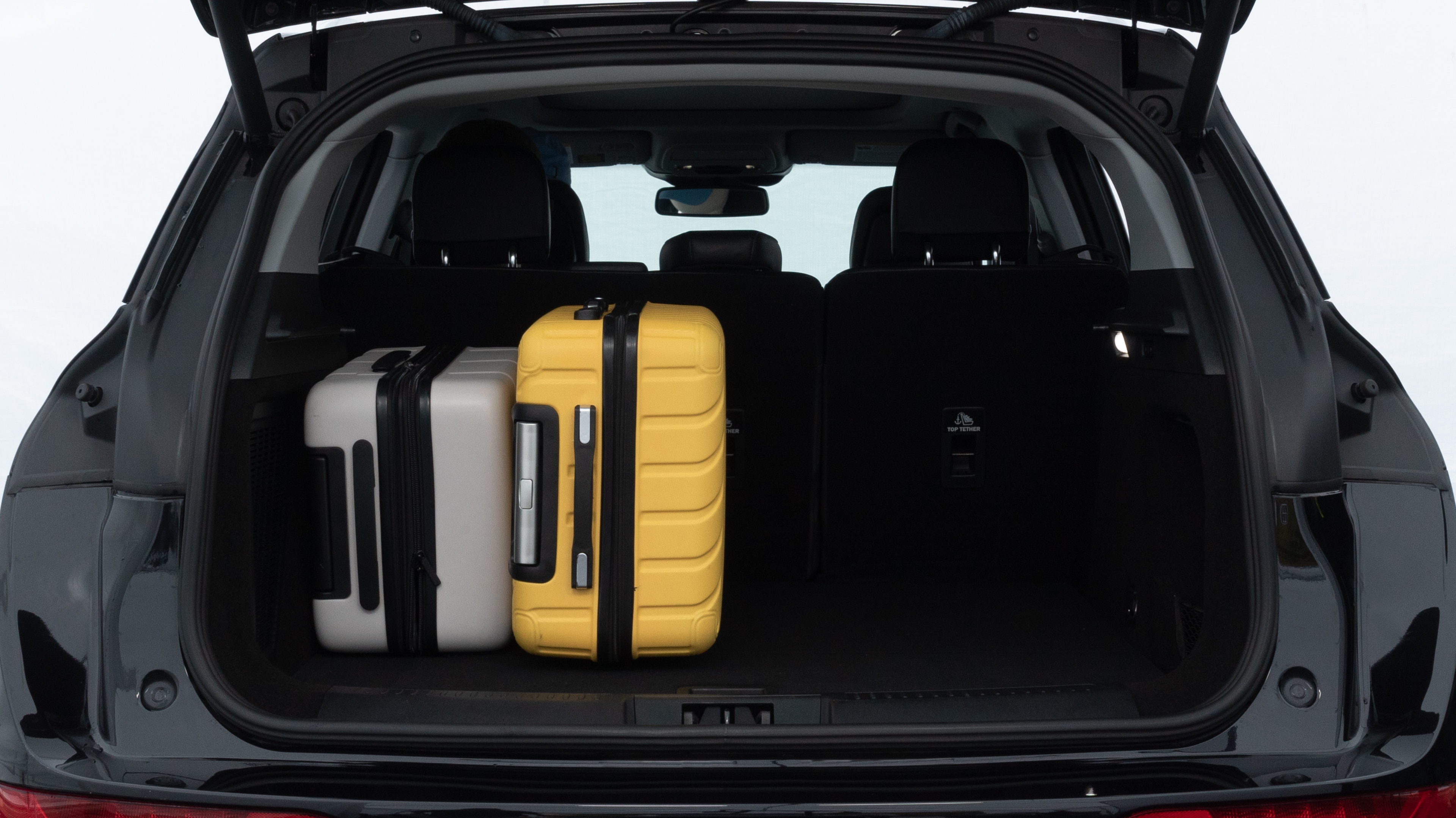 The trunk lid is open, showing full view of the trunk space. Two medium and two small suitcases are placed inside.