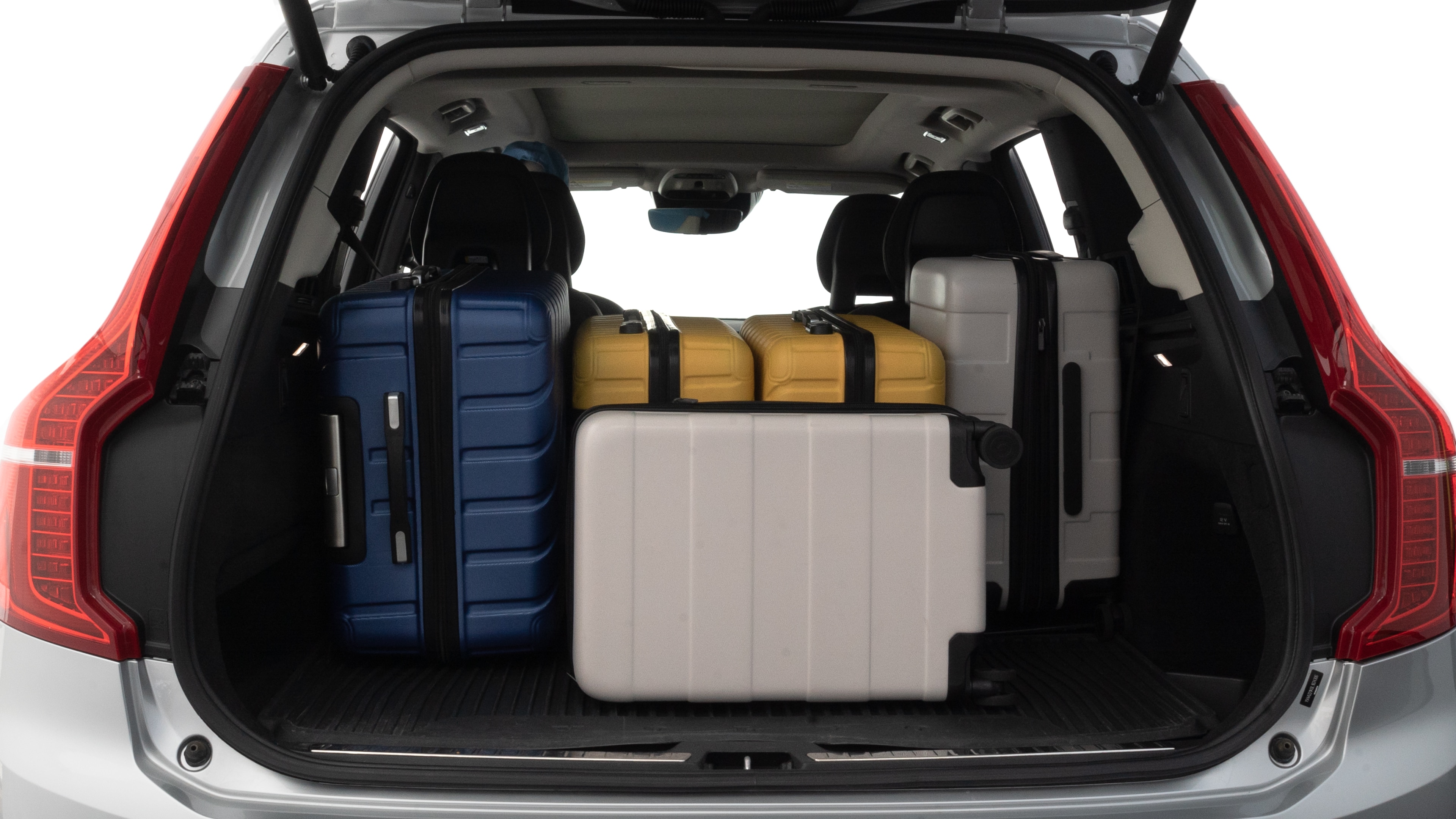 The trunk lid is open, showing full view of the trunk space. One large, two medium, and two small suitcases are placed inside.