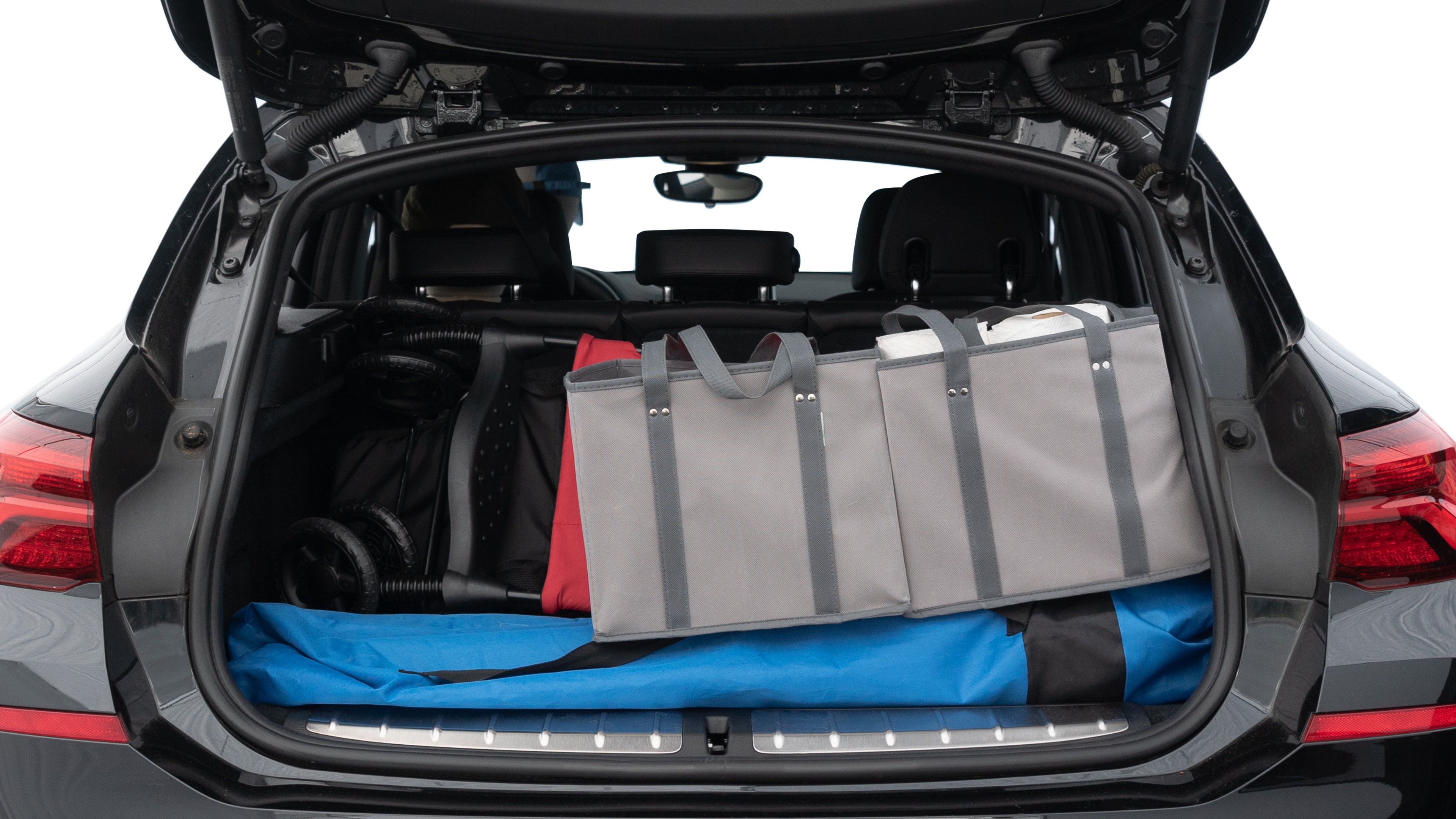 The trunk lid is open showing full view of the trunk. A baby stroller, three grocery carriers, two camping chairs in the carrying bag, and a set of golf clubs are placed inside.