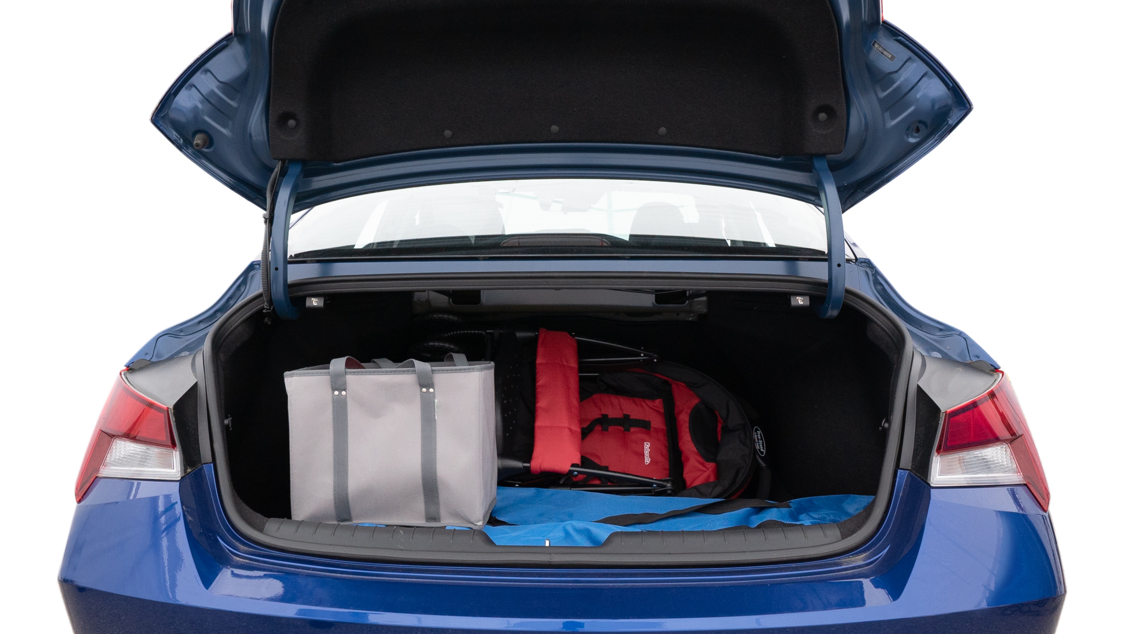 The trunk lid is open showing full view of the trunk. A baby stroller, three grocery carriers, two camping chairs in the carrying bag, and a set of golf clubs are placed inside.