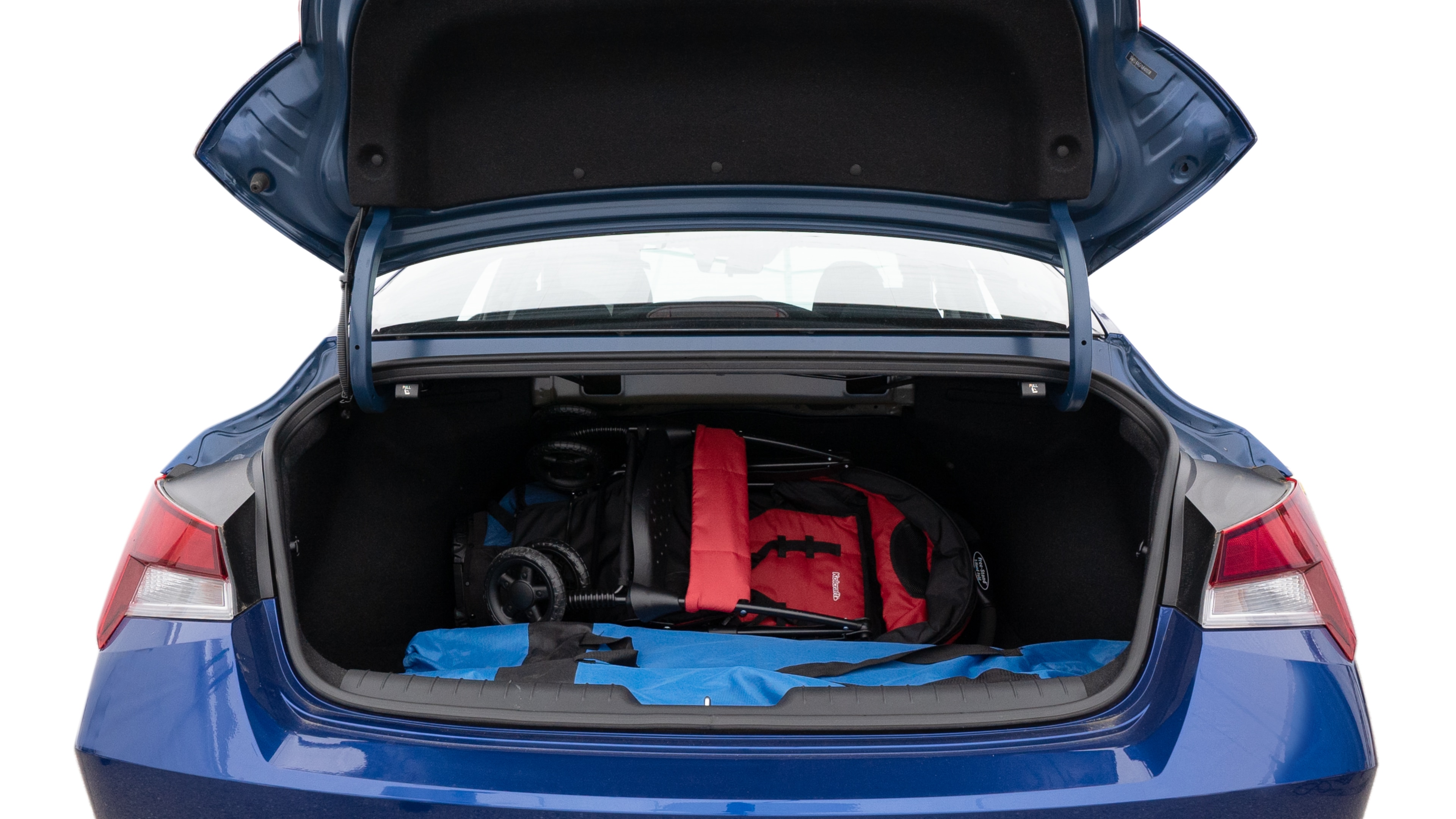 The trunk lid is open showing full view of the trunk. A baby stroller, three grocery carriers, two camping chairs in the carrying bag, and a set of golf clubs are placed inside.