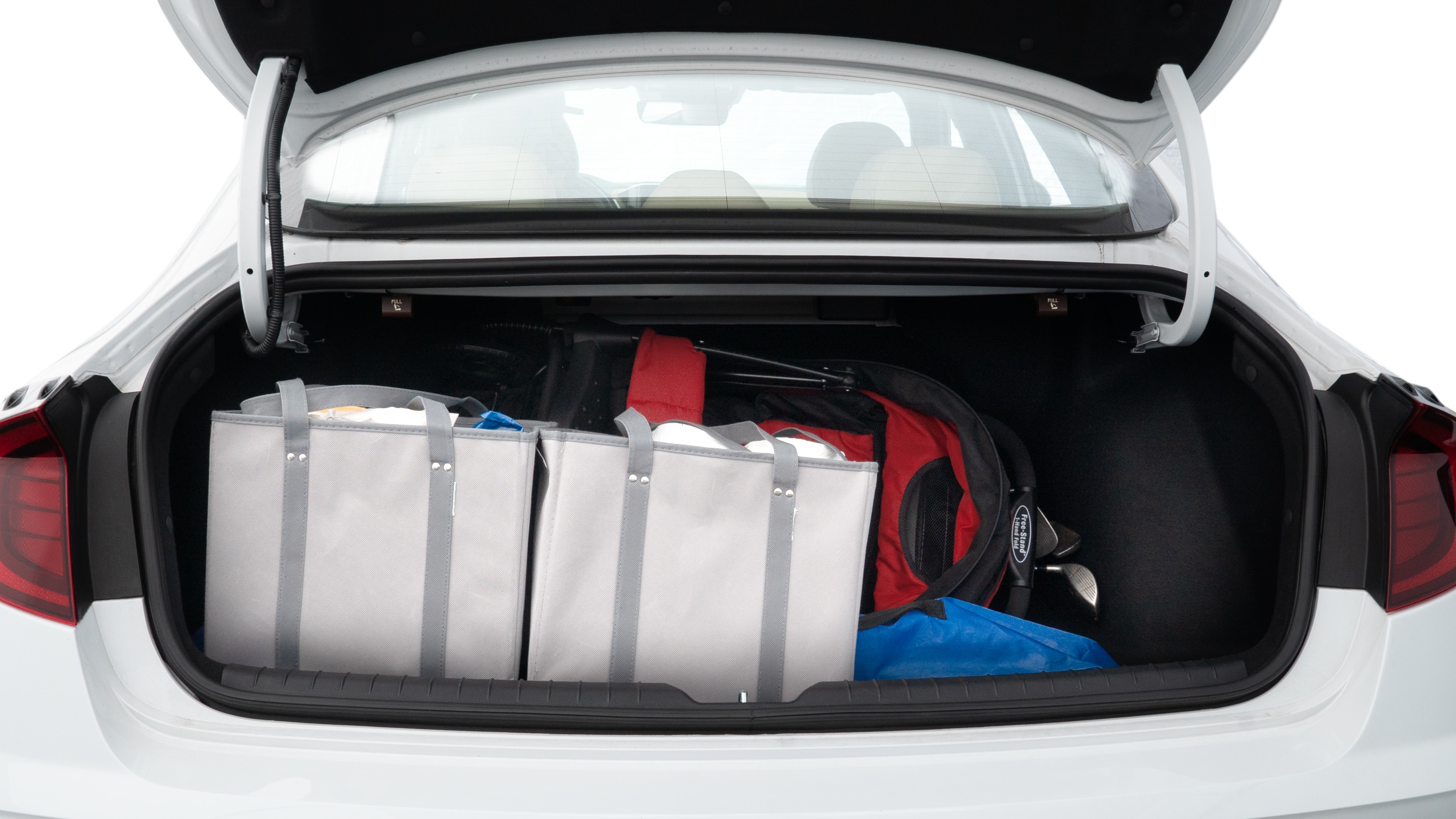 The trunk lid is open showing full view of the trunk. A baby stroller, three grocery carriers, two camping chairs in the carrying bag, and a set of golf clubs are placed inside.