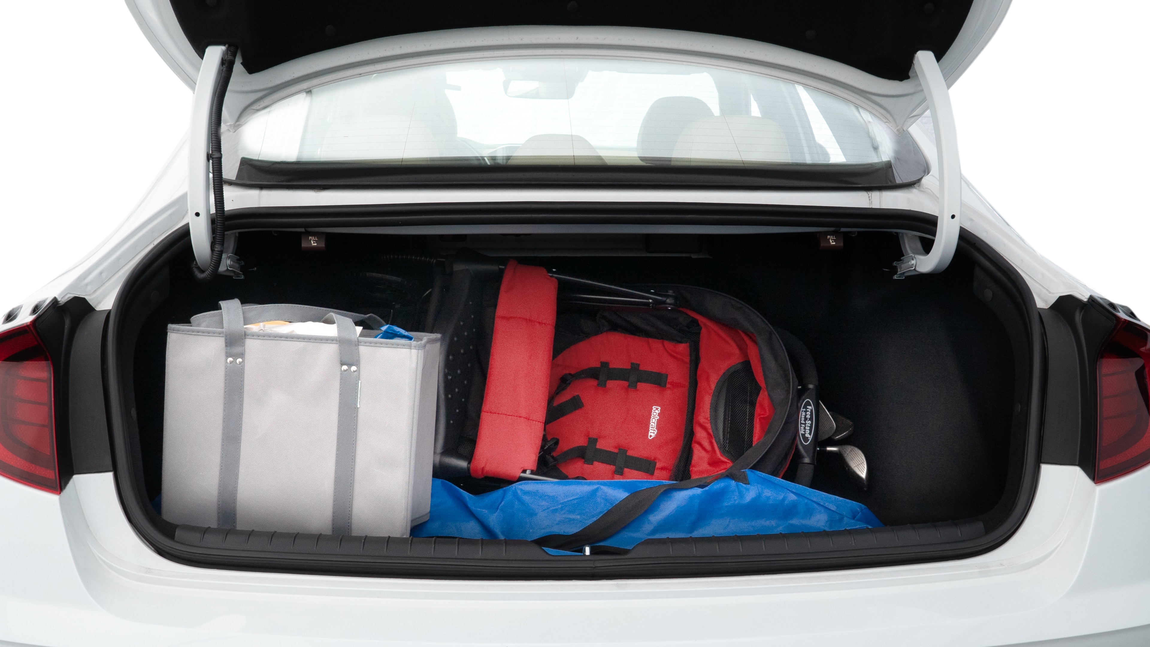 The trunk lid is open showing full view of the trunk. A baby stroller, three grocery carriers, two camping chairs in the carrying bag, and a set of golf clubs are placed inside.