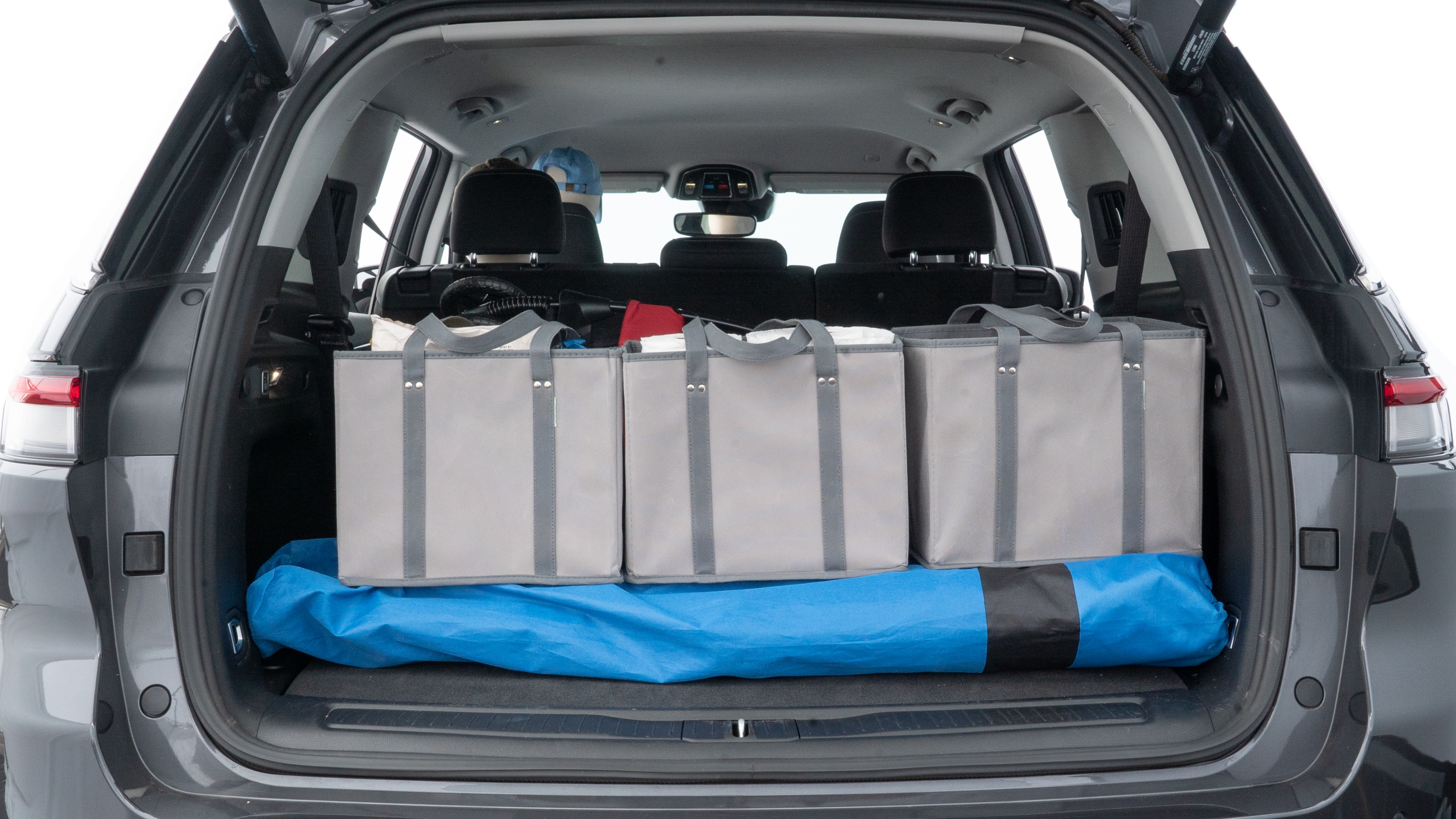 The trunk lid is open showing full view of the trunk. A baby stroller, three grocery carriers, two camping chairs in the carrying bag, and a set of golf clubs are placed inside.