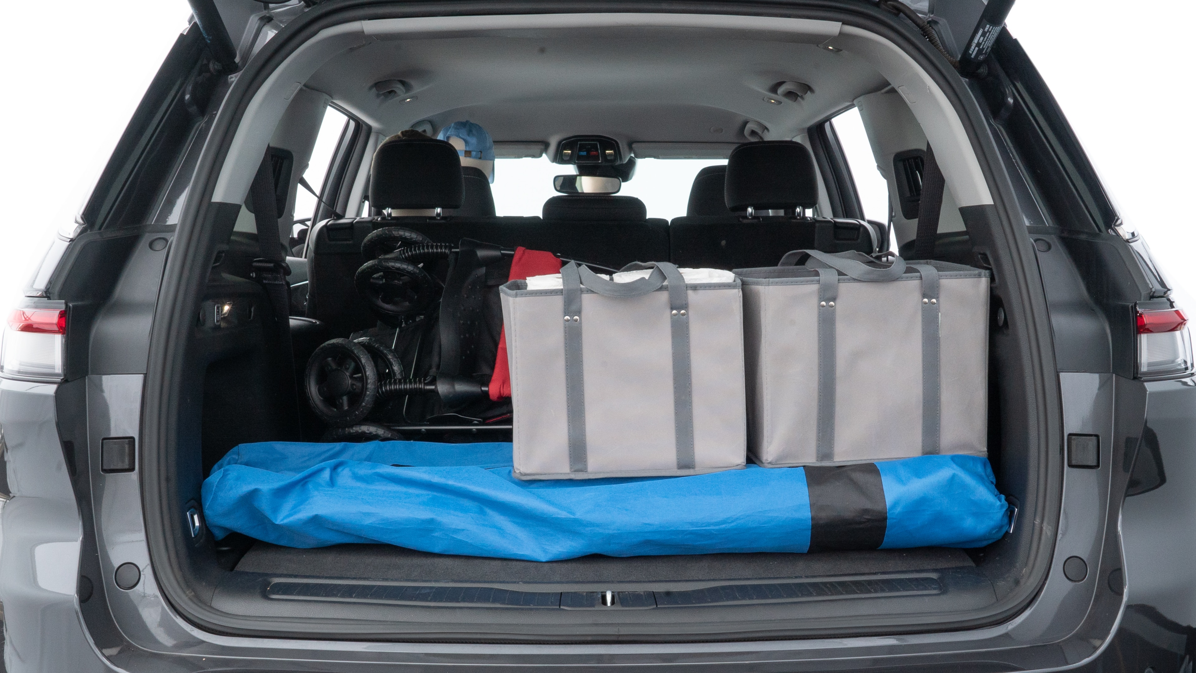 The trunk lid is open showing full view of the trunk. A baby stroller, three grocery carriers, two camping chairs in the carrying bag, and a set of golf clubs are placed inside.