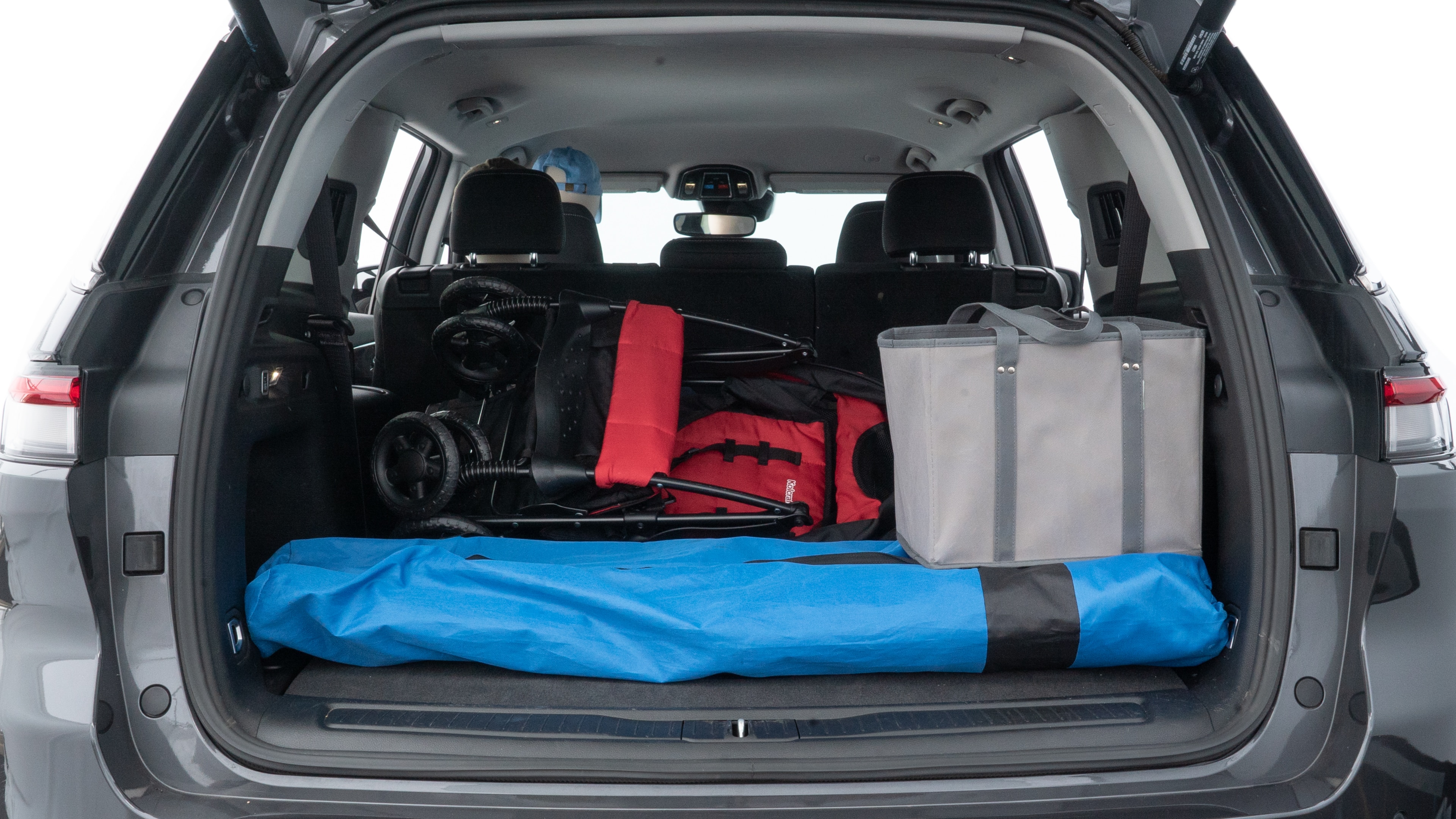 The trunk lid is open showing full view of the trunk. A baby stroller, three grocery carriers, two camping chairs in the carrying bag, and a set of golf clubs are placed inside.