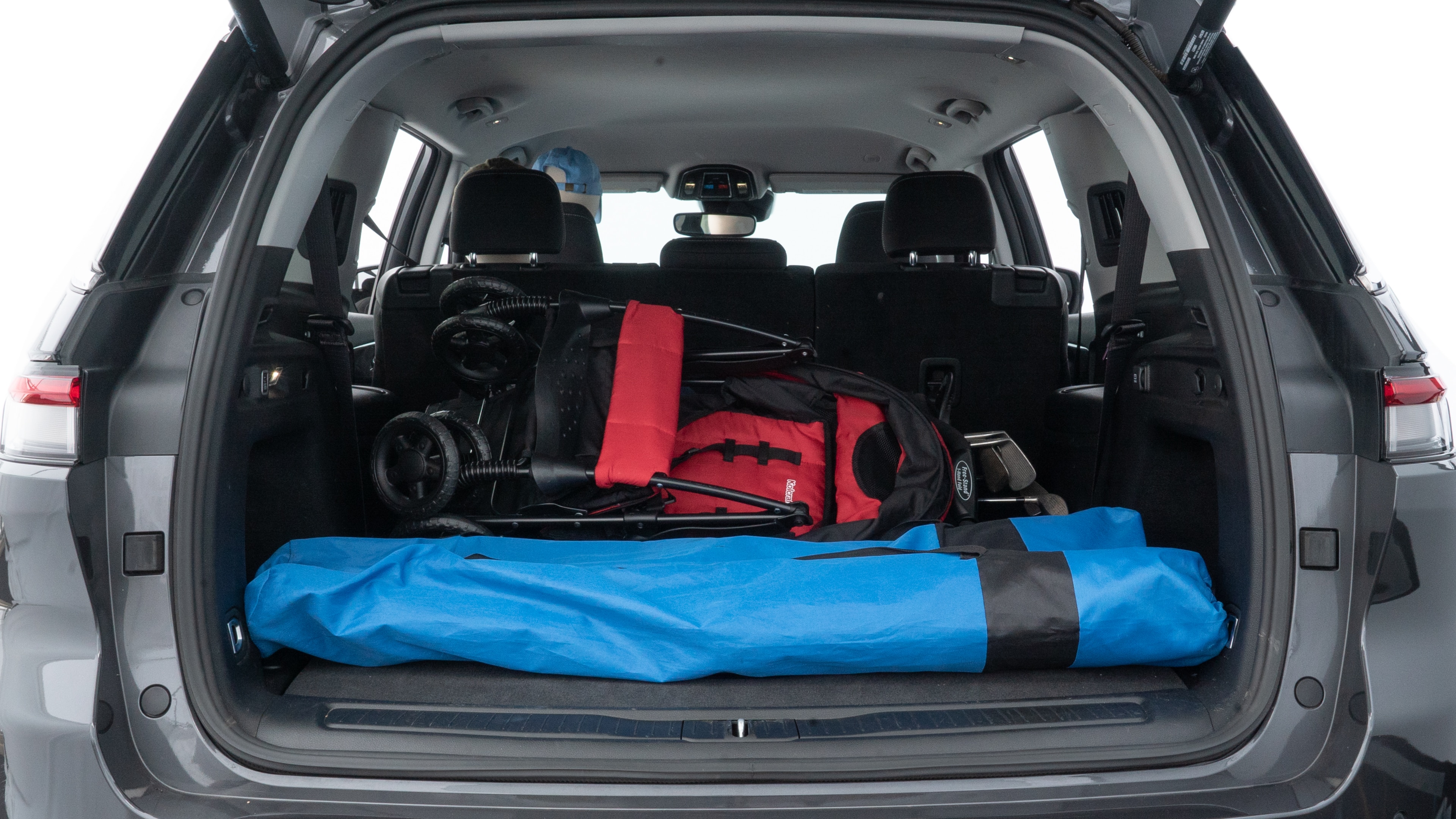 The trunk lid is open showing full view of the trunk. A baby stroller, three grocery carriers, two camping chairs in the carrying bag, and a set of golf clubs are placed inside.