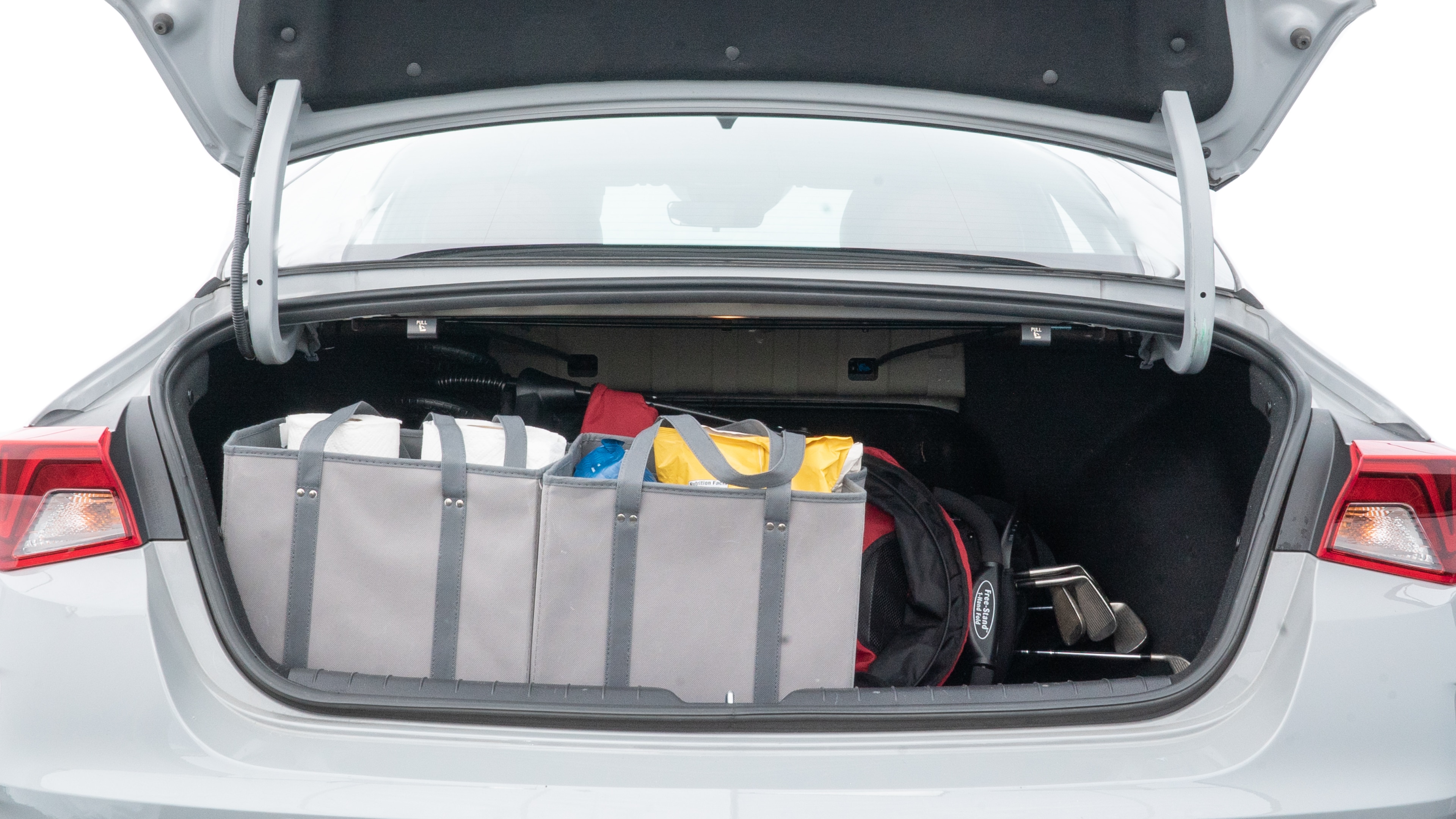 The trunk lid is open showing full view of the trunk. A baby stroller, three grocery carriers, two camping chairs in the carrying bag, and a set of golf clubs are placed inside.