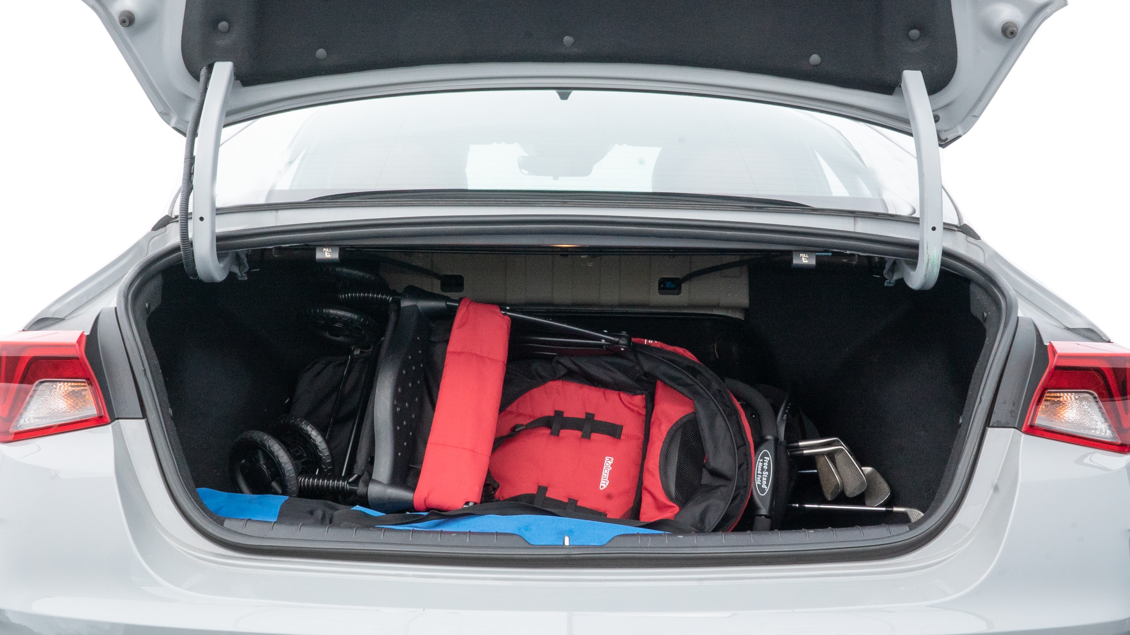 The trunk lid is open showing full view of the trunk. A baby stroller, three grocery carriers, two camping chairs in the carrying bag, and a set of golf clubs are placed inside.