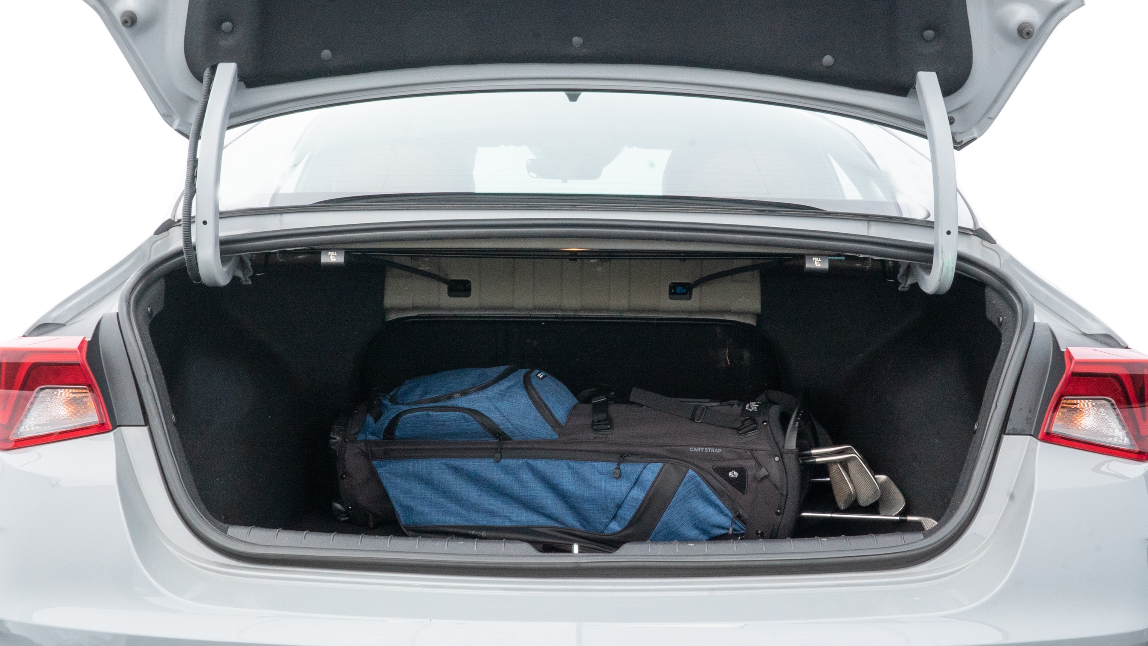 The trunk lid is open showing full view of the trunk. A baby stroller, three grocery carriers, two camping chairs in the carrying bag, and a set of golf clubs are placed inside.