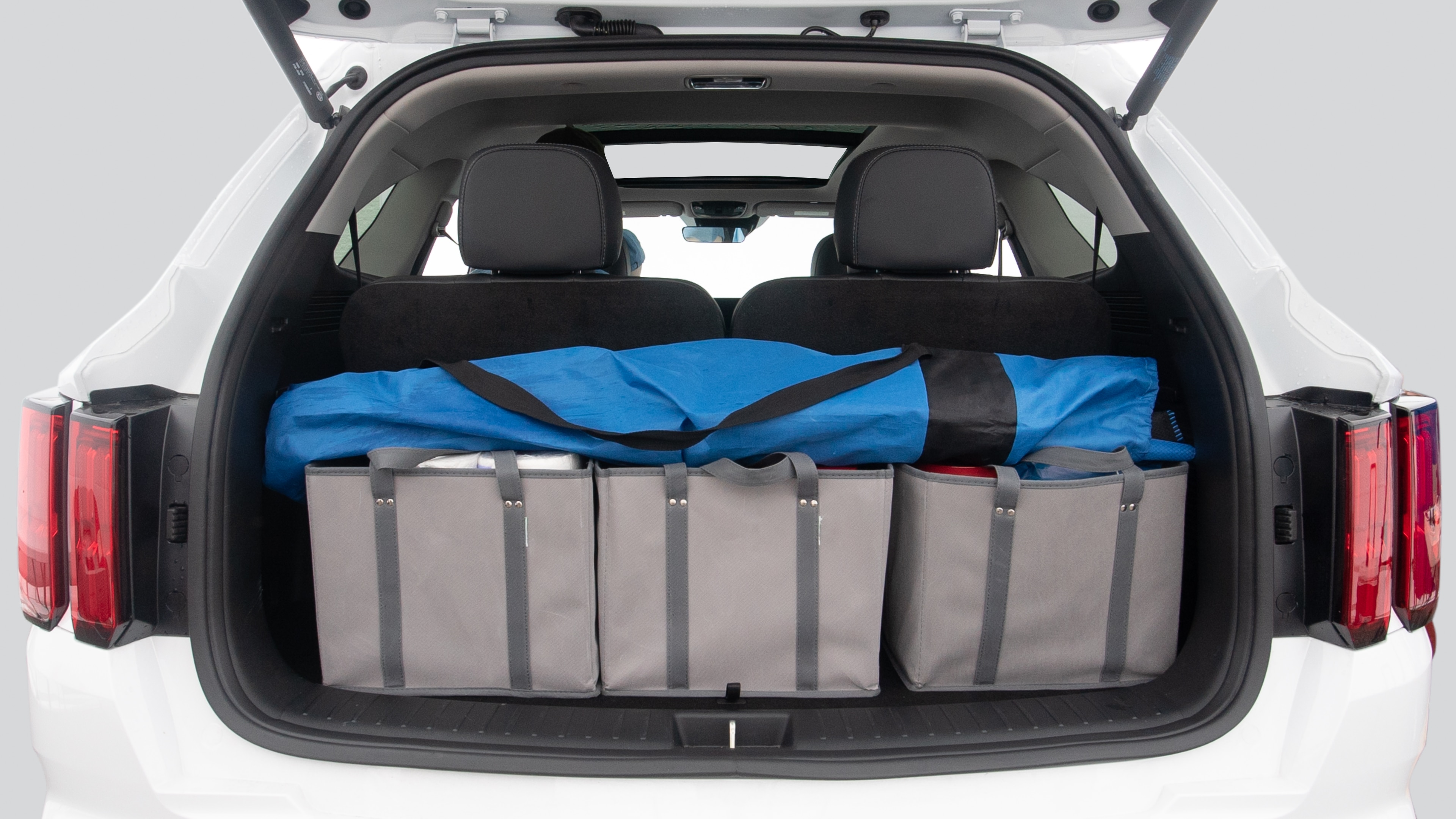 The trunk lid is open showing full view of the trunk. Three grocery carriers, and two camping chairs in the carrying bag are placed inside.