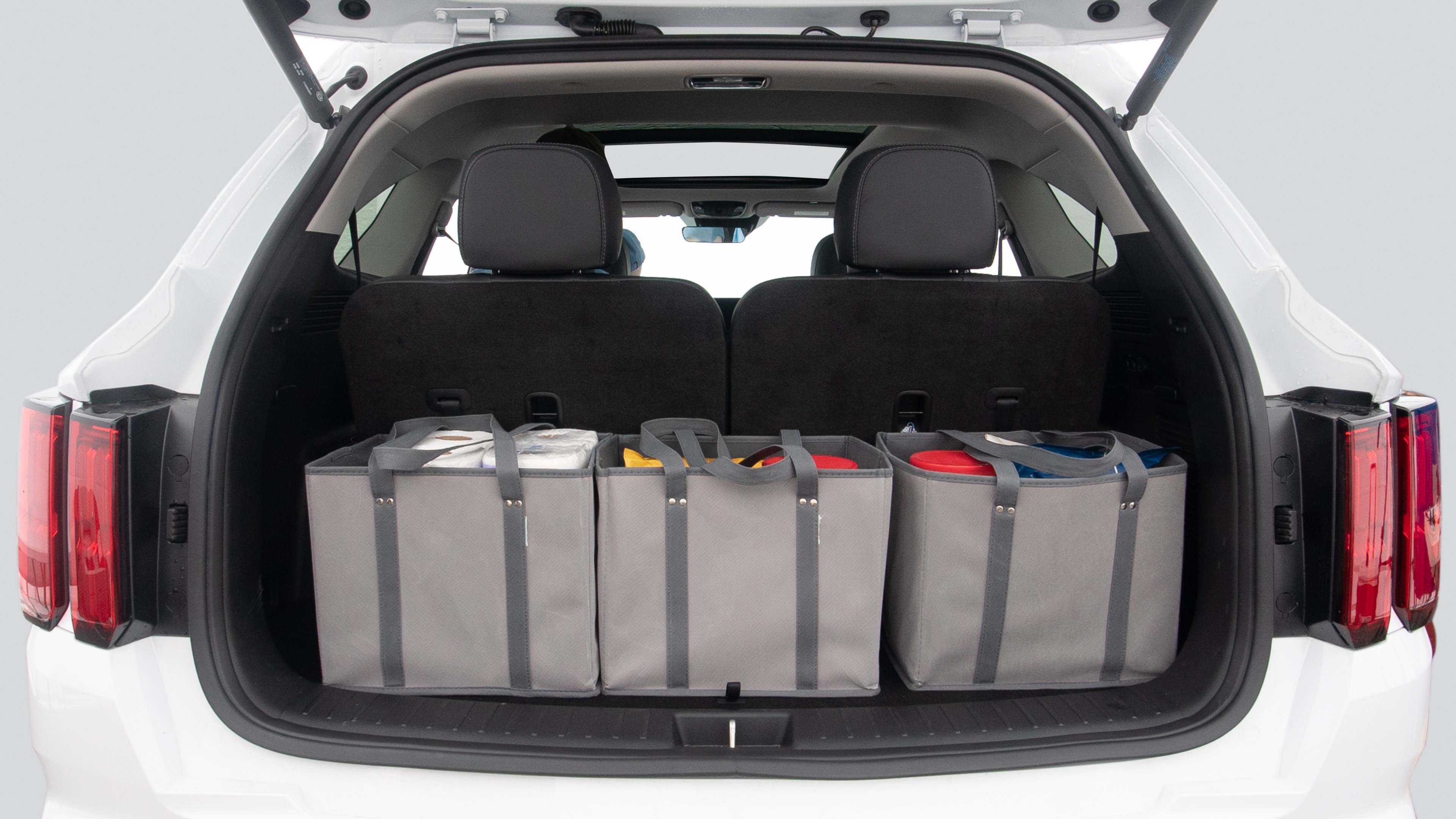The trunk lid is open showing full view of the trunk. Three grocery carriers, and two camping chairs in the carrying bag are placed inside.