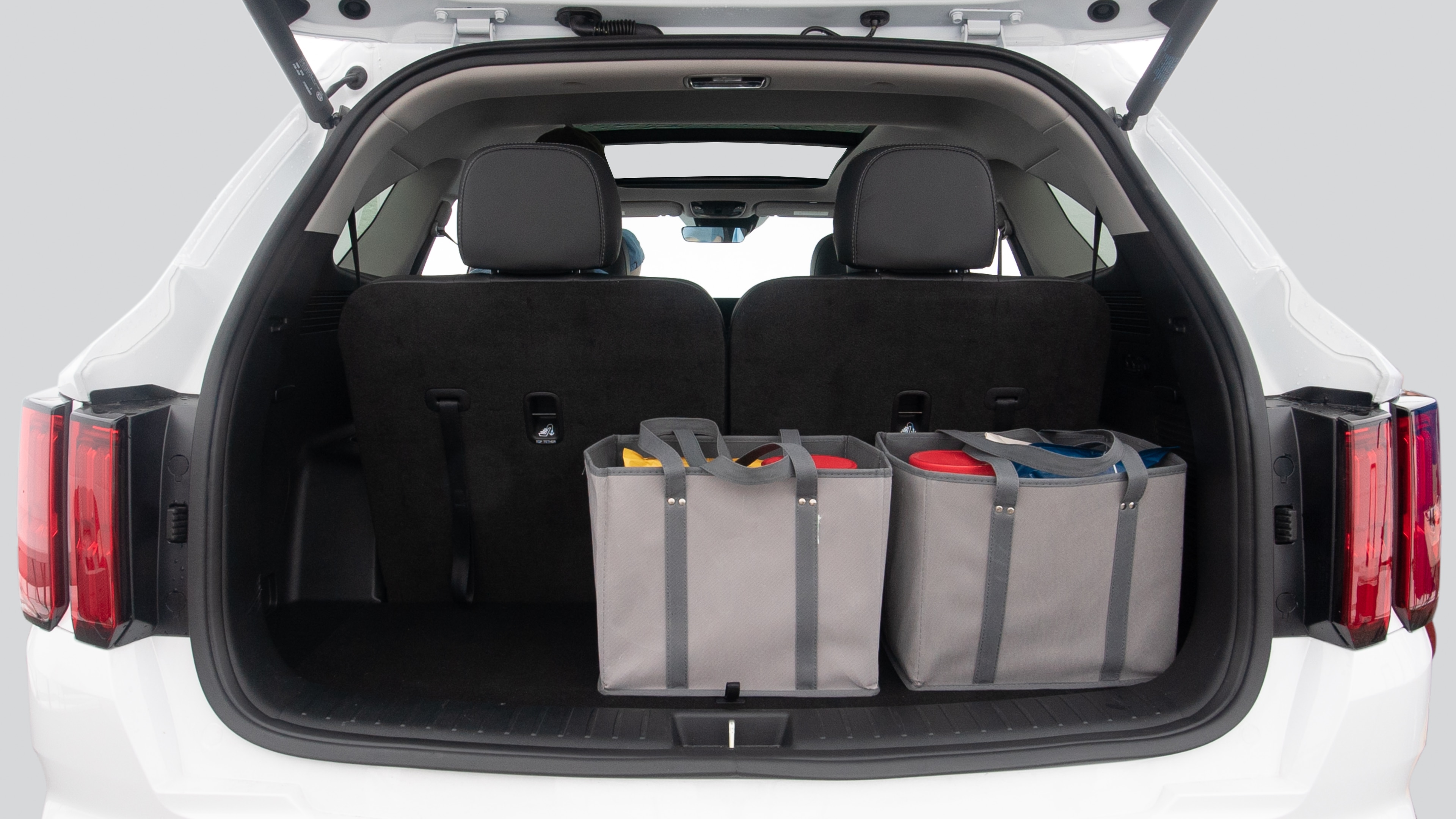 The trunk lid is open showing full view of the trunk. Three grocery carriers, and two camping chairs in the carrying bag are placed inside.