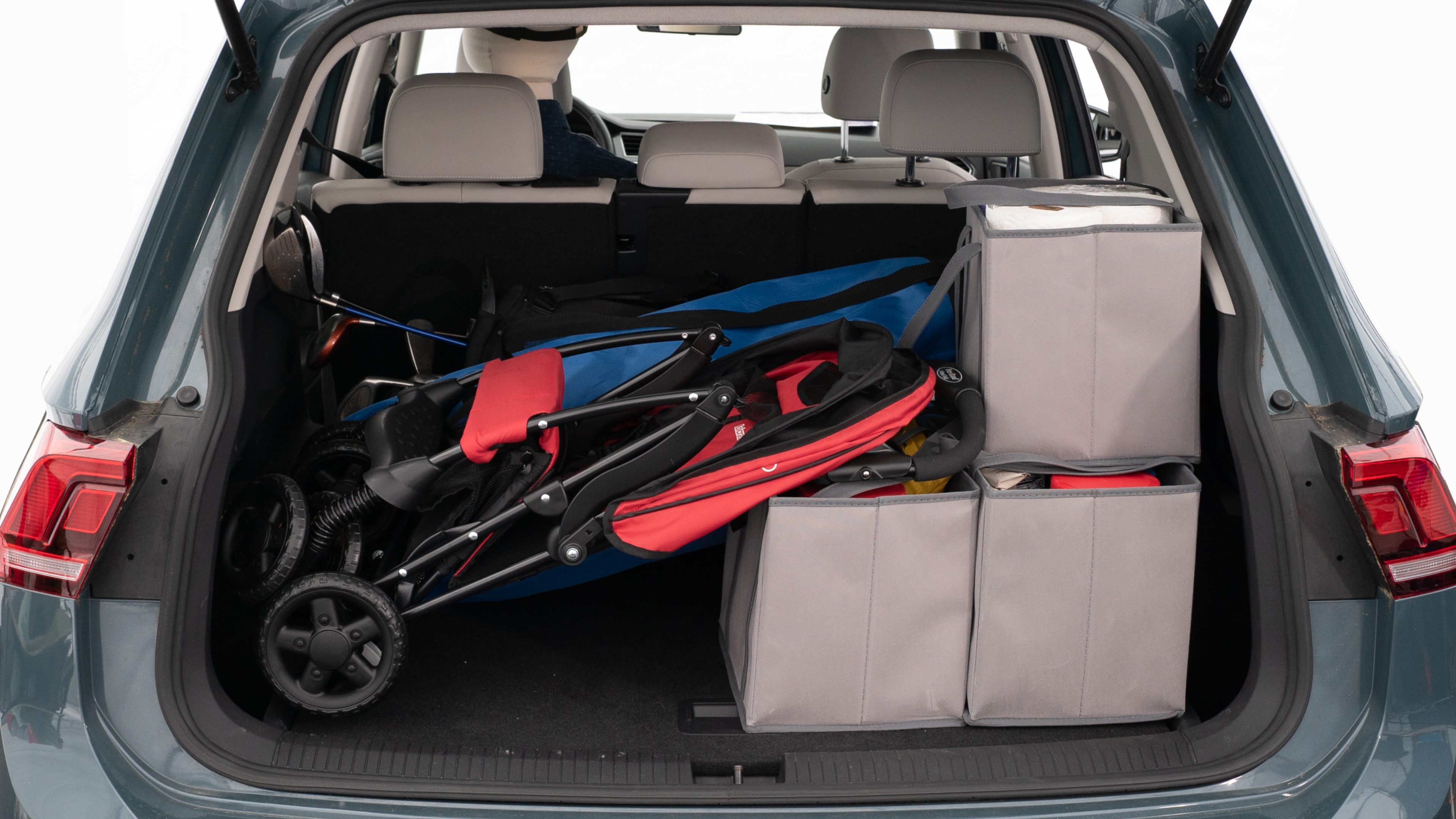 The trunk lid is open showing full view of the trunk. A baby stroller, three grocery carriers, two camping chairs in the carrying bag, and a set of golf clubs are placed inside.