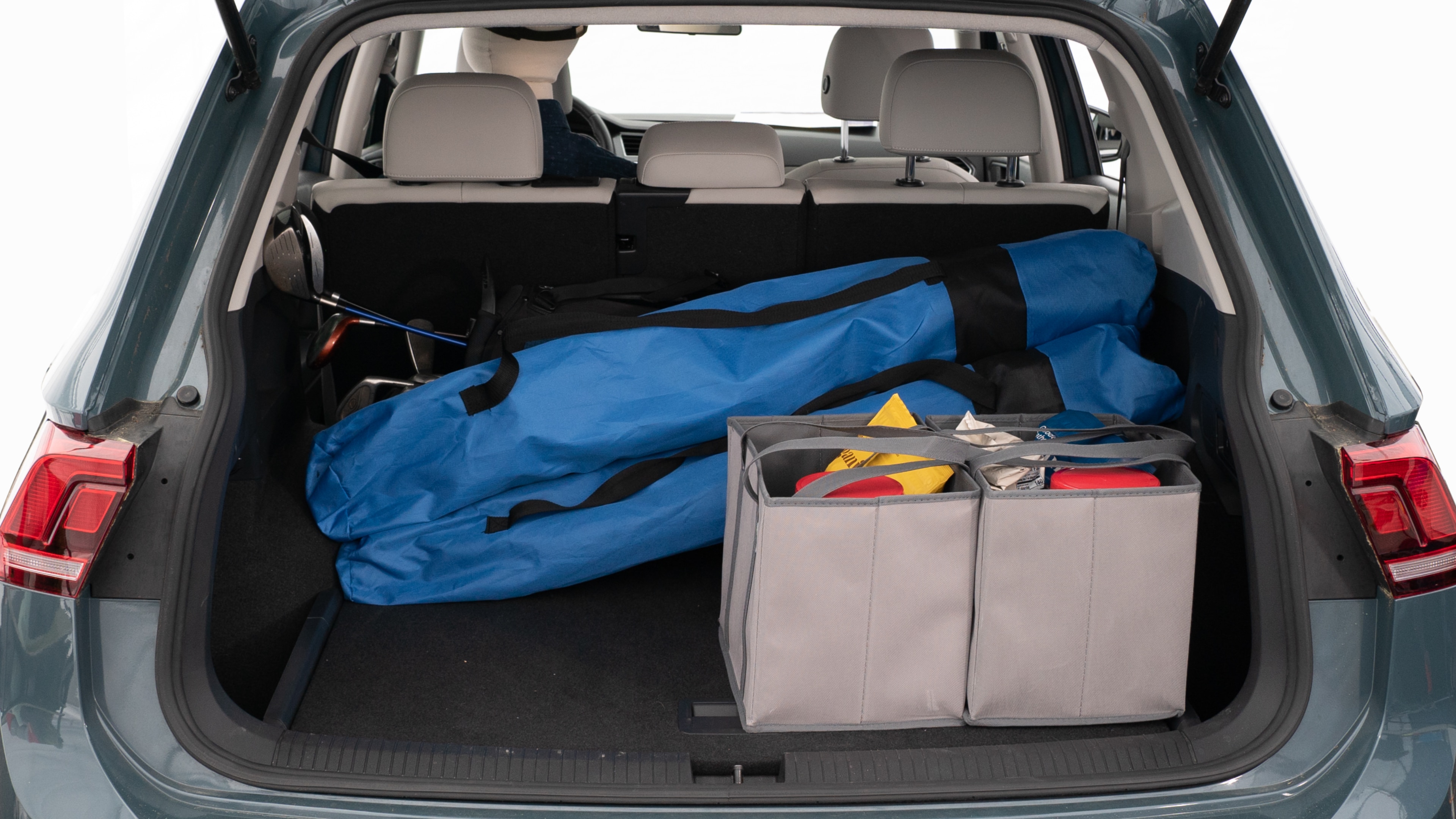 The trunk lid is open showing full view of the trunk. A baby stroller, three grocery carriers, two camping chairs in the carrying bag, and a set of golf clubs are placed inside.